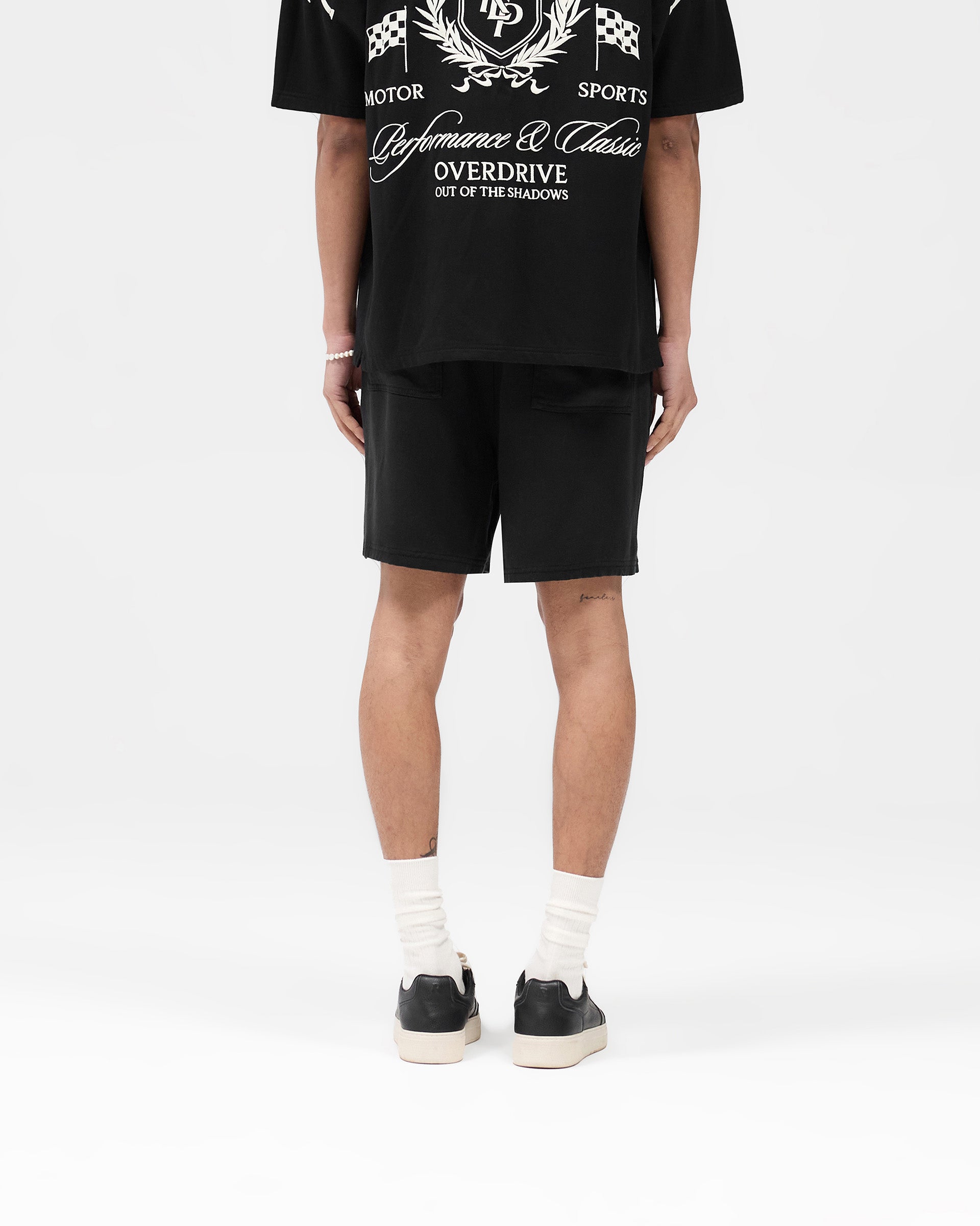 Man wearing black shorts on a plain white background | Represent Crest Short in Jet Black | Shorts with forest green crest embroidery and elasticated waistband | SS25 Shorts | Represent Clo