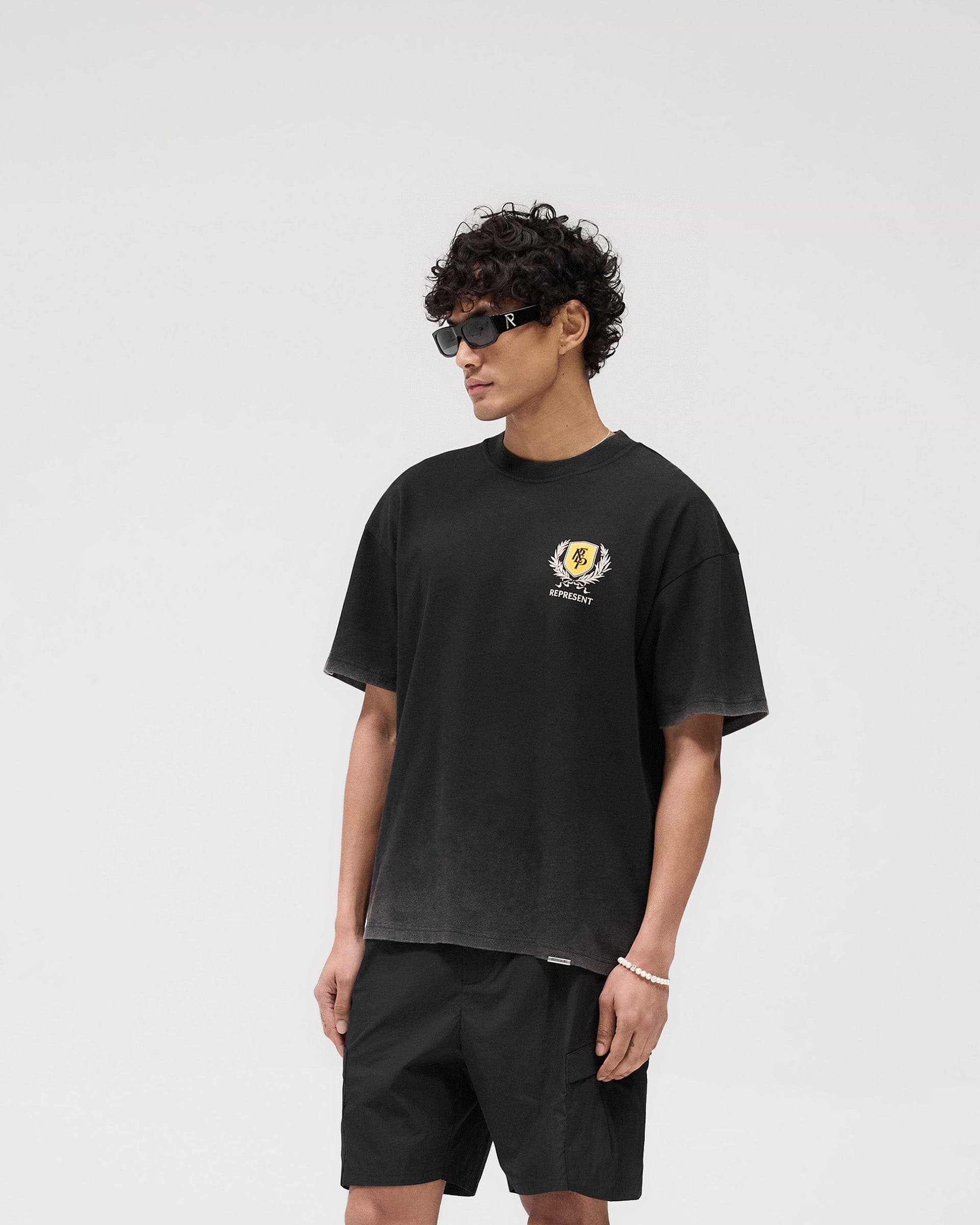 Man wearing a vintage black graphic t-shirt on a plain white background | Crest T-Shirt in Vintage Black | Oversized fit tee with puff and screen print graphics | SS25 T-Shirts | Represent Clo