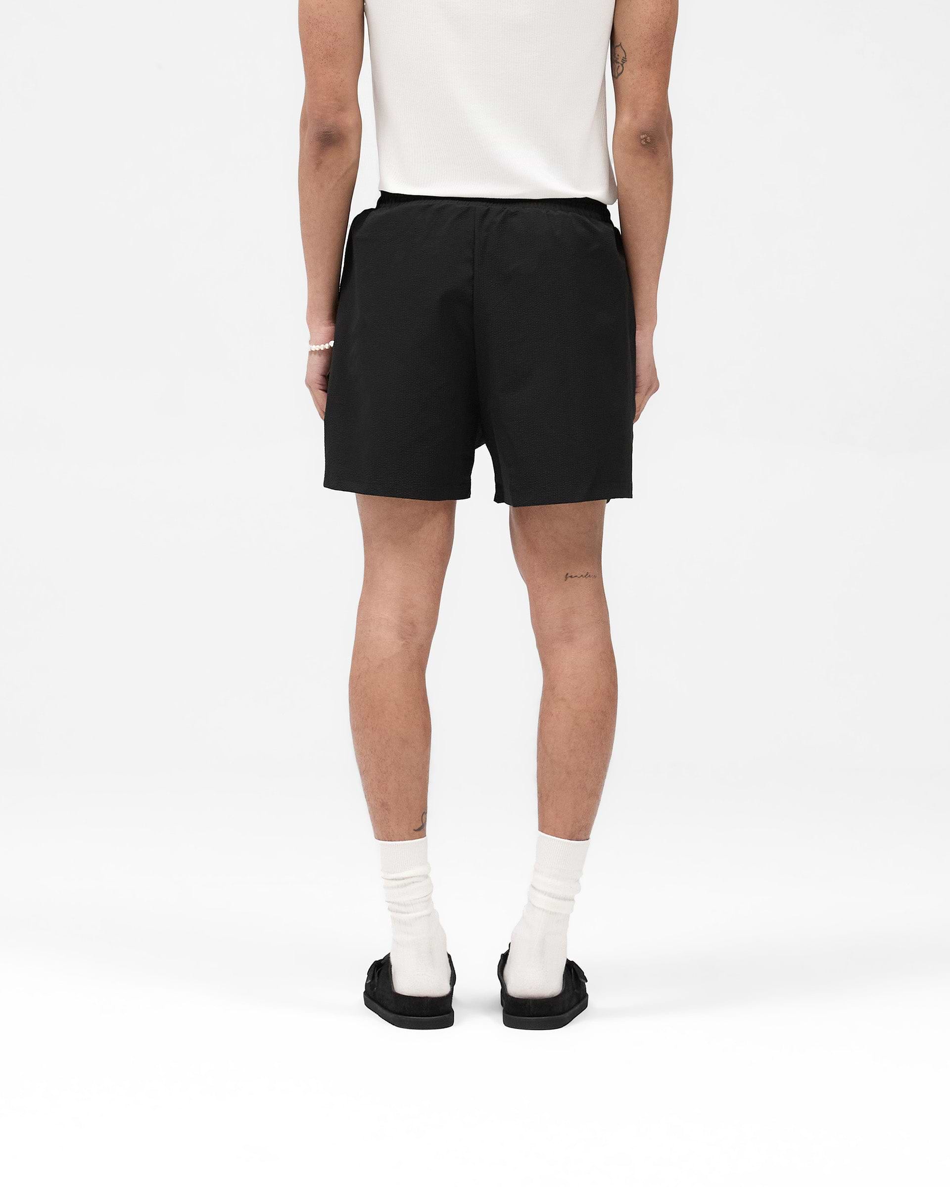 Man wearing black swim shorts on a plain white background | Seersucker Smart Swim Short in Black | Swim shorts with internal lining and embroidered logo | SS25 Shorts | Represent Clo