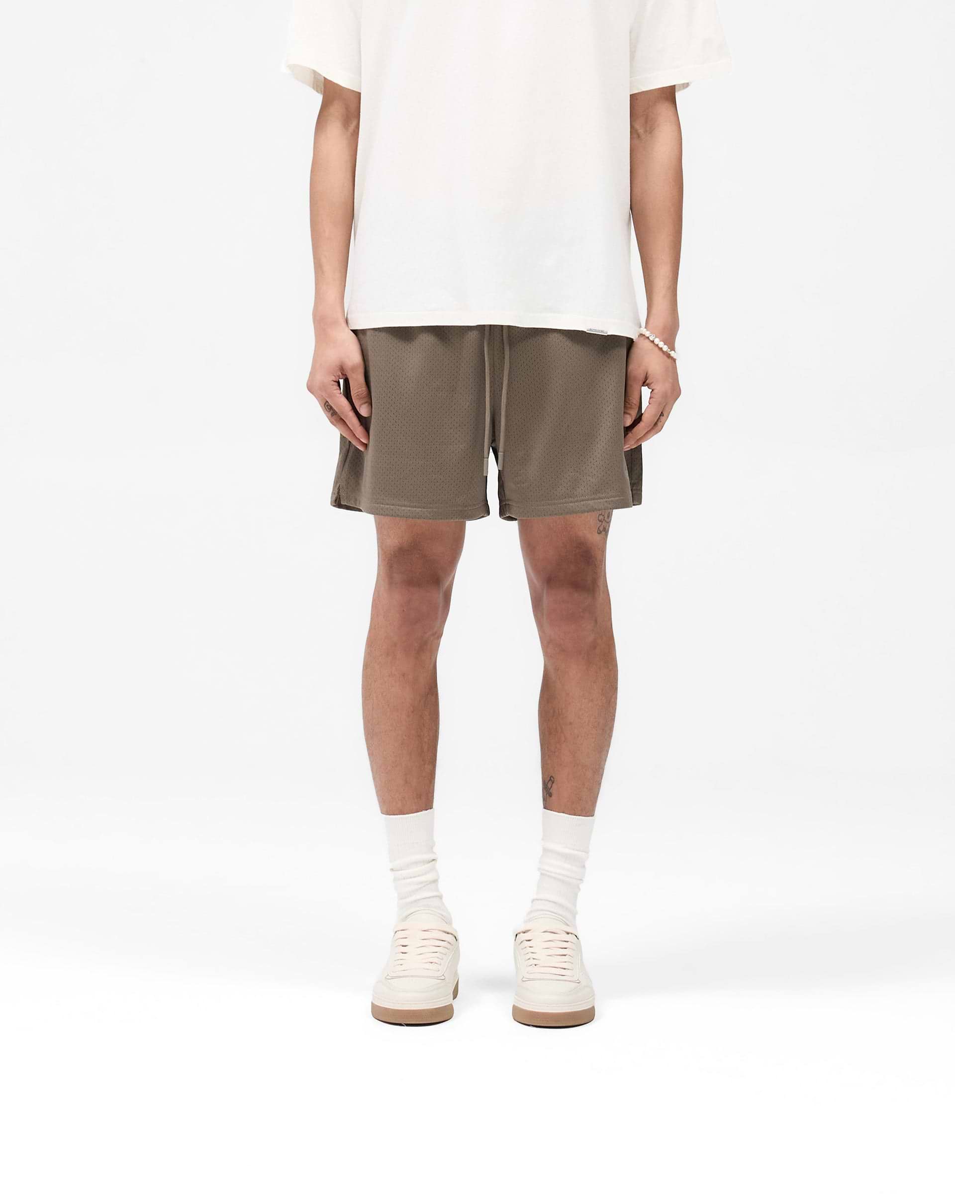 Man wearing stone mesh shorts on a plain white background | Mesh Short in Stone | Mesh shorts with zip pockets and internal drawcord | SS25 Shorts | Represent Clo
