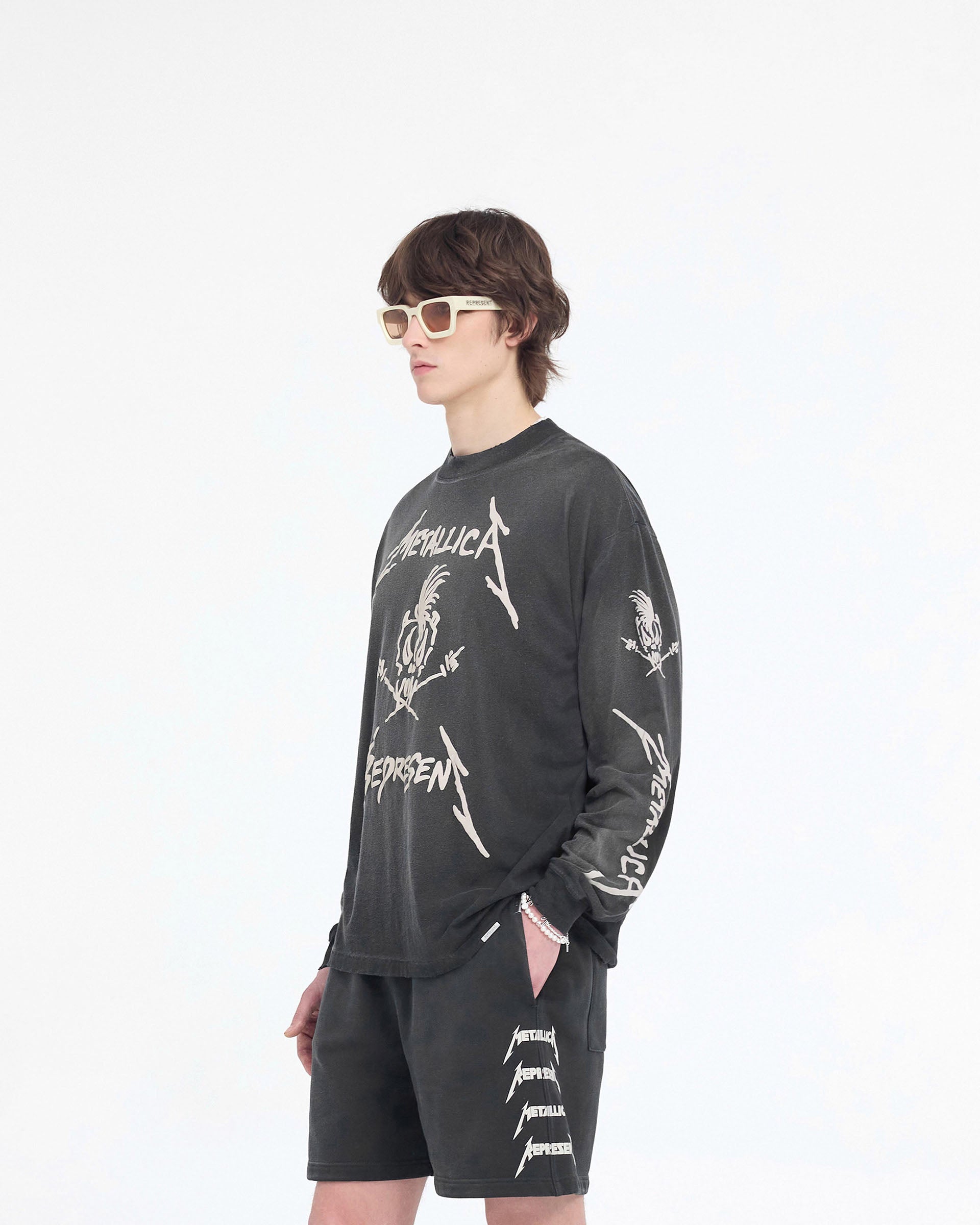 Man wearing a black long sleeve t-shirt on a plain white background | Represent X Metallica Garage Inc Long Sleeve T-Shirt in Stained Black | Vintage style t-shirt with puff print and ribbed cuffs | SS24 T-Shirts | Represent Clo