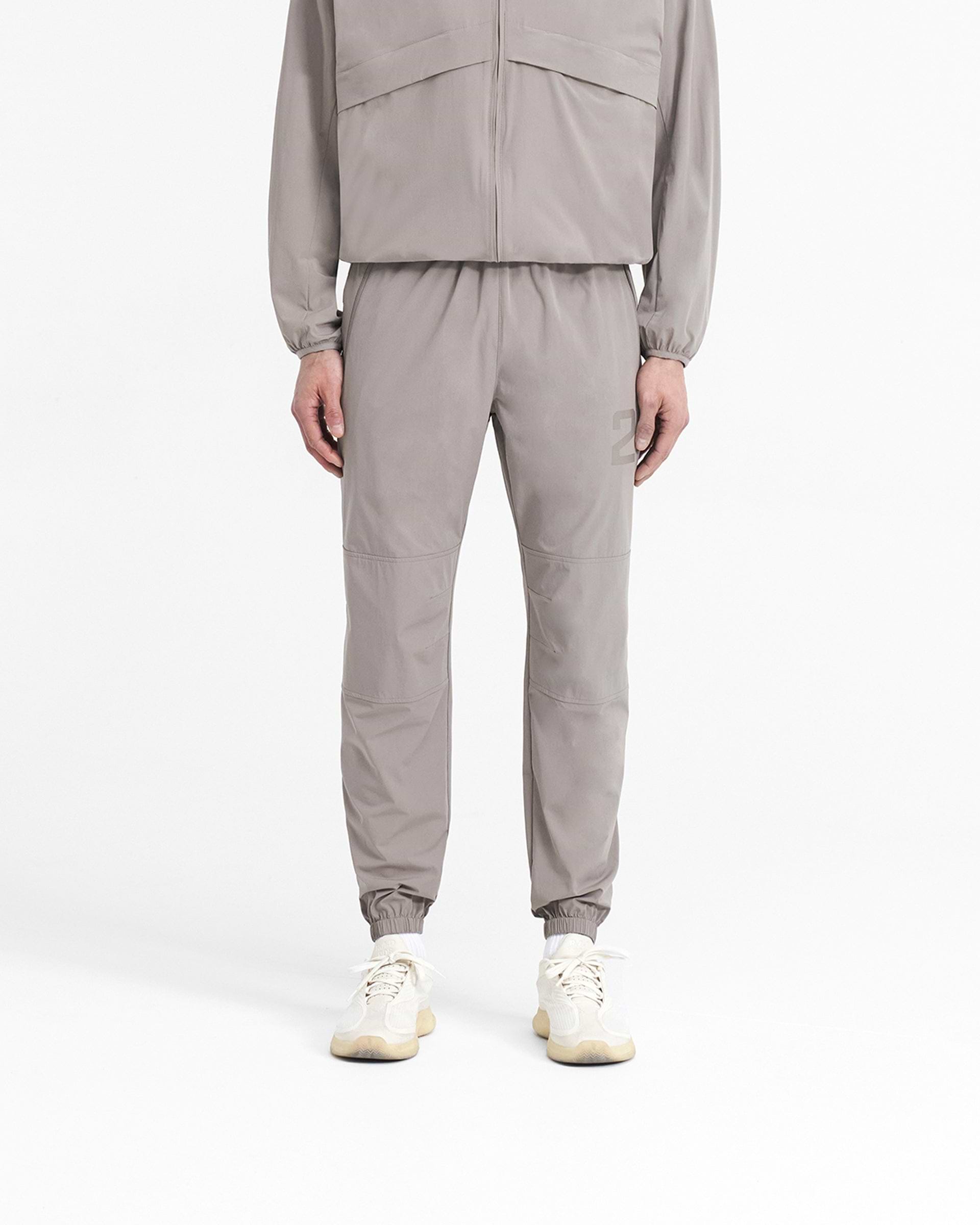 Man wearing grey training pants on a plain white background | 247 Training Pant in Cinder | Pants with elasticated waistband and zip pockets | 247 Pants | Represent Clo