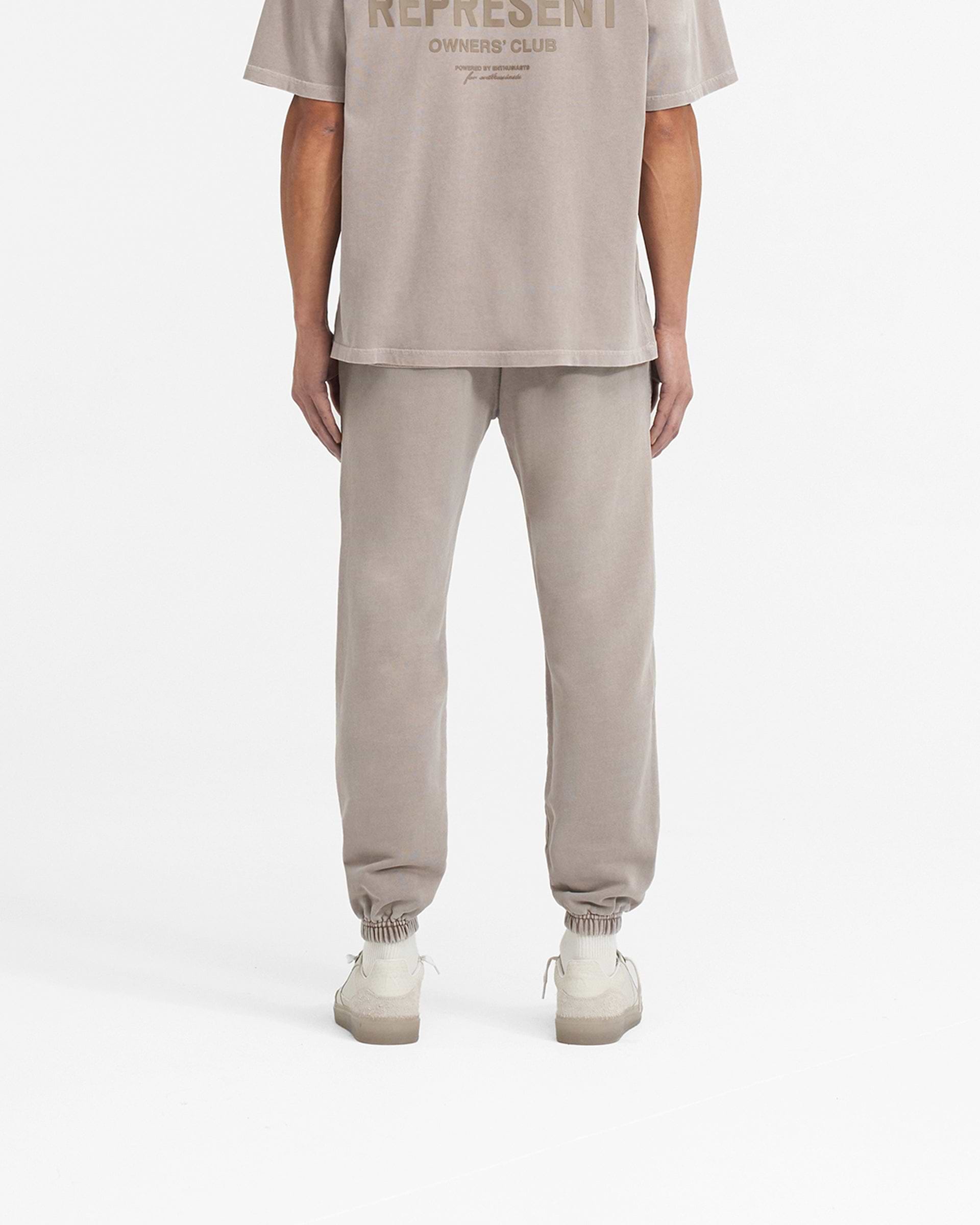 Man wearing mushroom coloured sweatpants on a plain white background | Represent Owners Club Sweatpant in Mushroom | Sweatpants with elasticated waistband and high build tonal branding | Owners Club Pants | Represent Clo