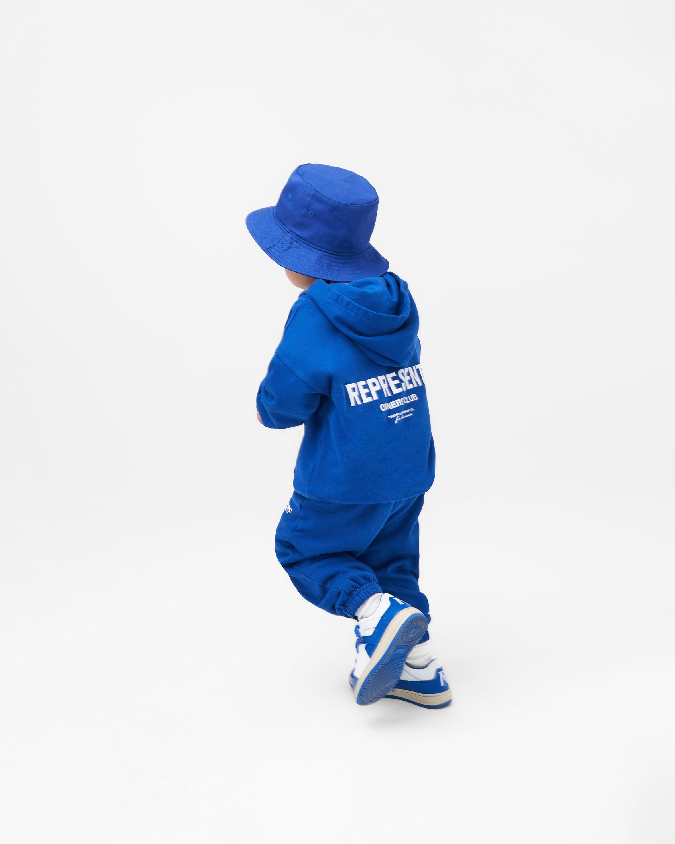 Child wearing blue sweatpants on a plain white background | Represent Mini Owners Club Sweatpants in Cobalt | Kids sweatpants with elasticated waistband and cuffs | Owners Club Pants | Represent Clo