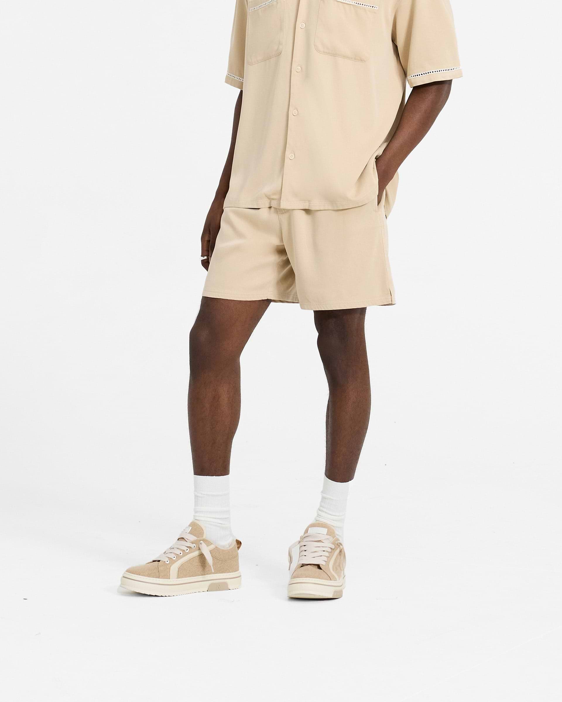 Man wearing relaxed fit mens brown shorts on a plain white background | Resort Shorts in Latte | Shorts with elasticated waistband and drawcord | SC24 Shorts | Represent Clo