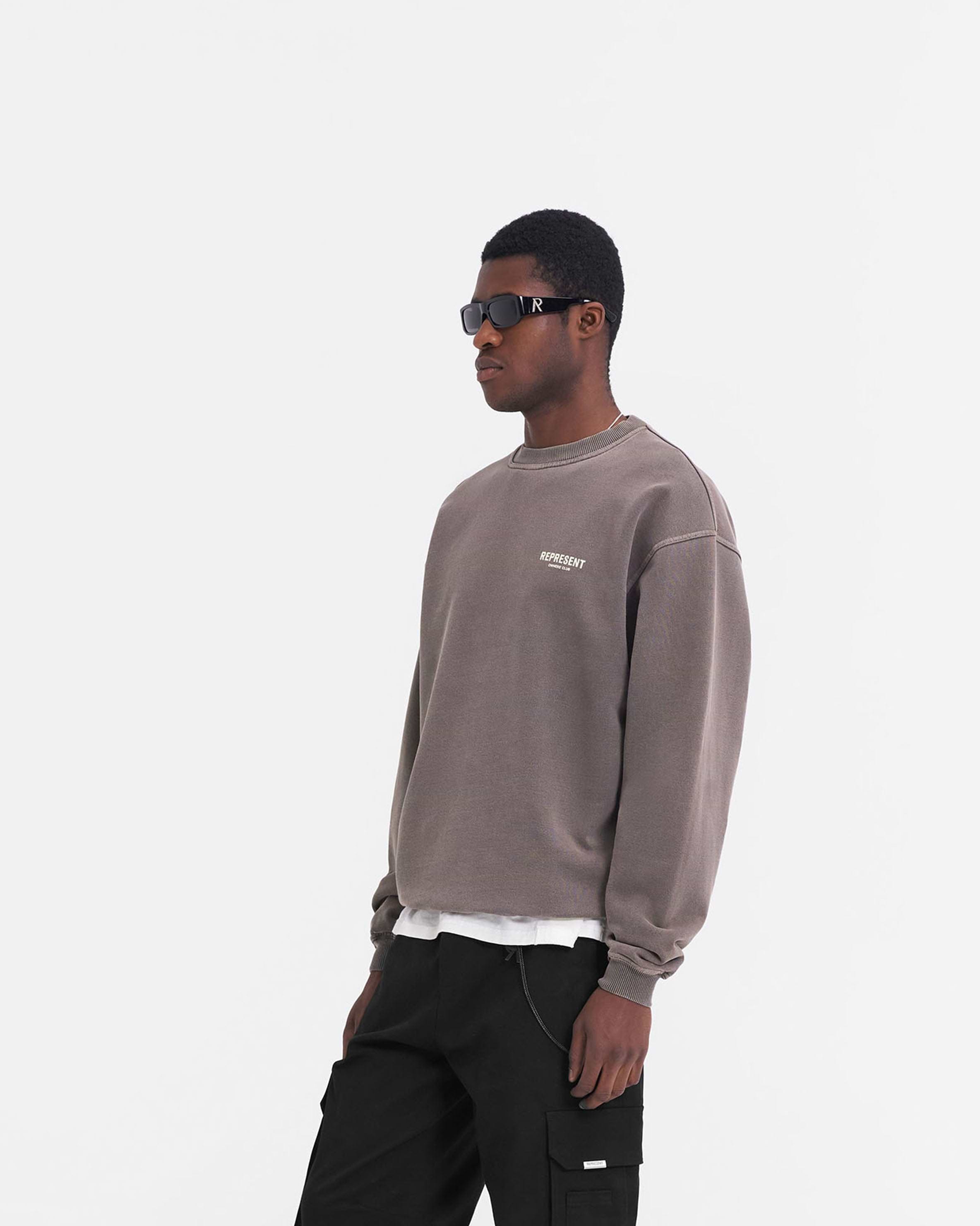 Man wearing an oversized grey sweater on a plain white background | Represent Owners Club Sweater in Fog | Oversized crewneck sweater with branding | Owners Club Sweaters | Represent Clo