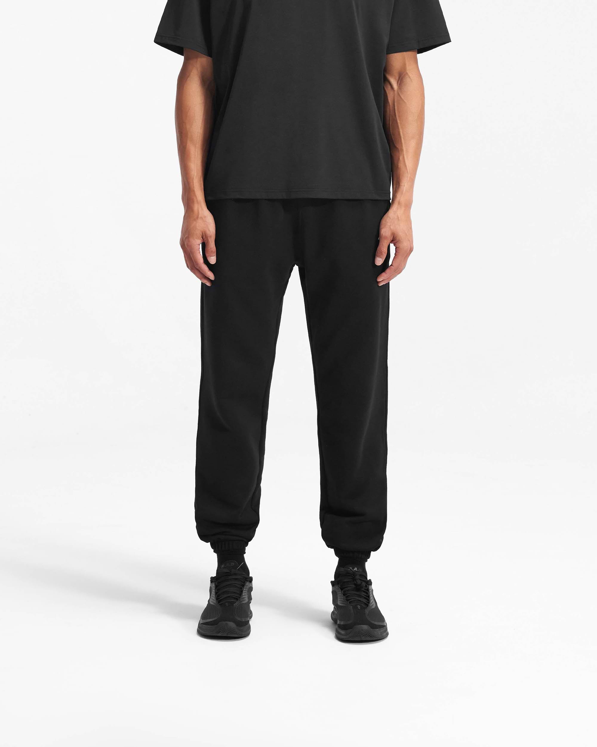 Man wearing black sweatpants on a plain white background | Team 247 Sweatpant in Black | Sweatpants with elasticated cuffs and drawcord waist | 247 Pants | Represent Clo