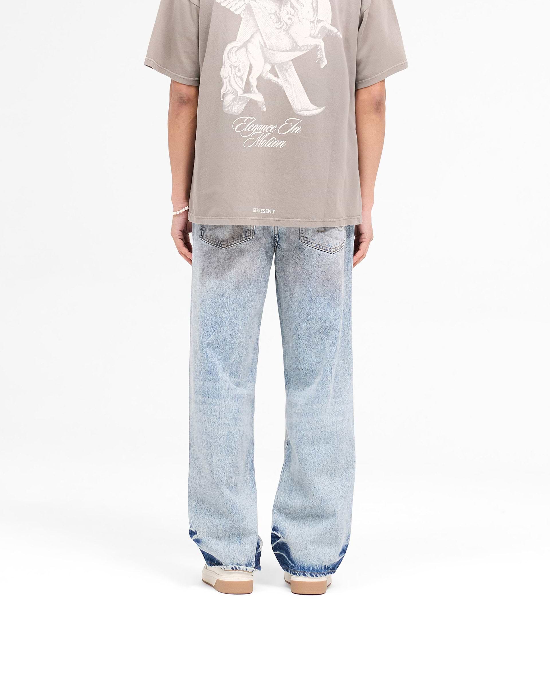 Model wearing mens blue denim jeans on a plain white background | R3 Baggy Denim in Mechanic Blue | Baggy fit denim with patched dye and initial embroidery | SS25 Denim | Represent Clo