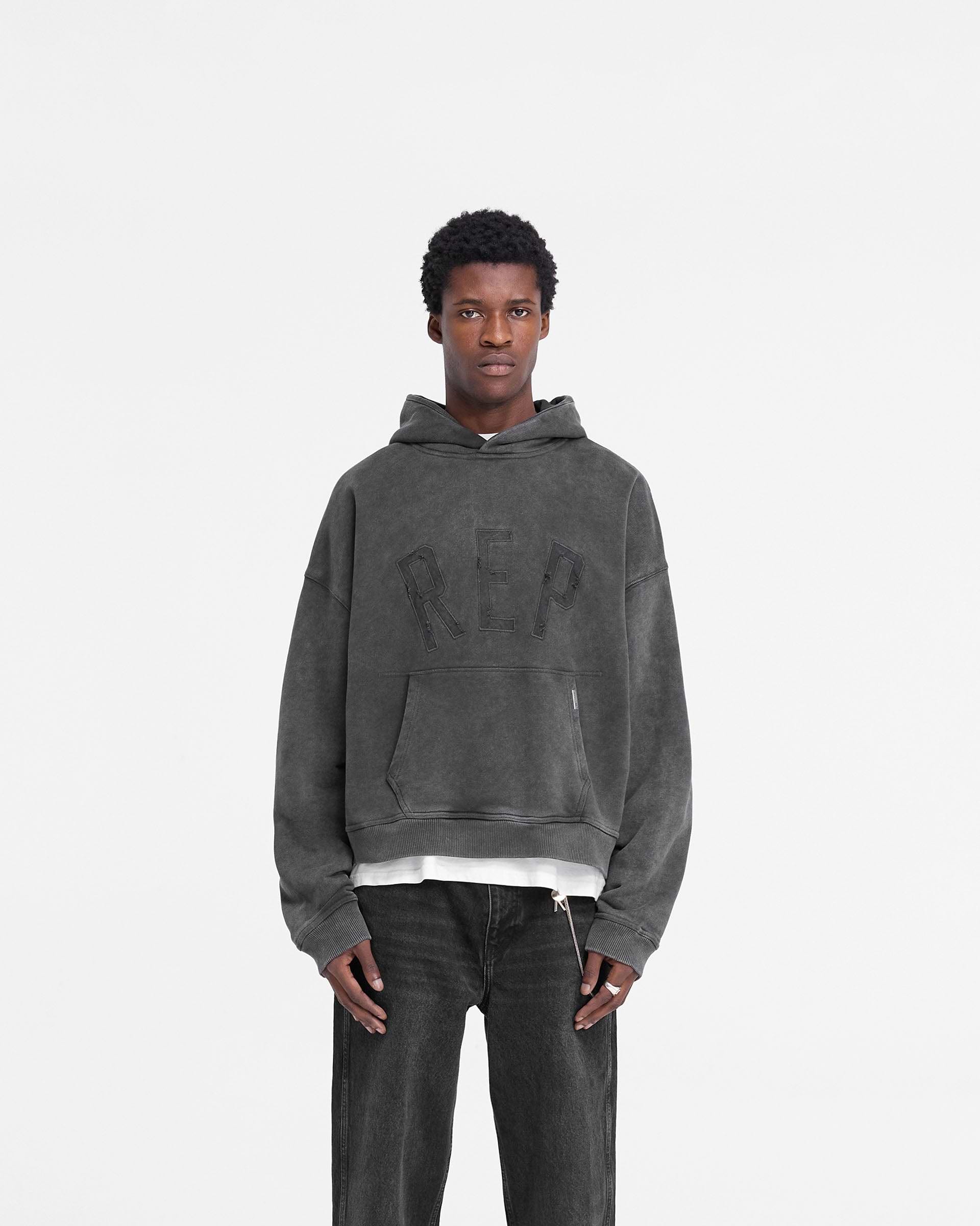 Man wearing a black hoodie on a plain white background | Rep Applique Hoodie in Vintage Black | Oversized boxy fit hoodie with distressed applique logo | FW24 Hoodies | Represent Clo
