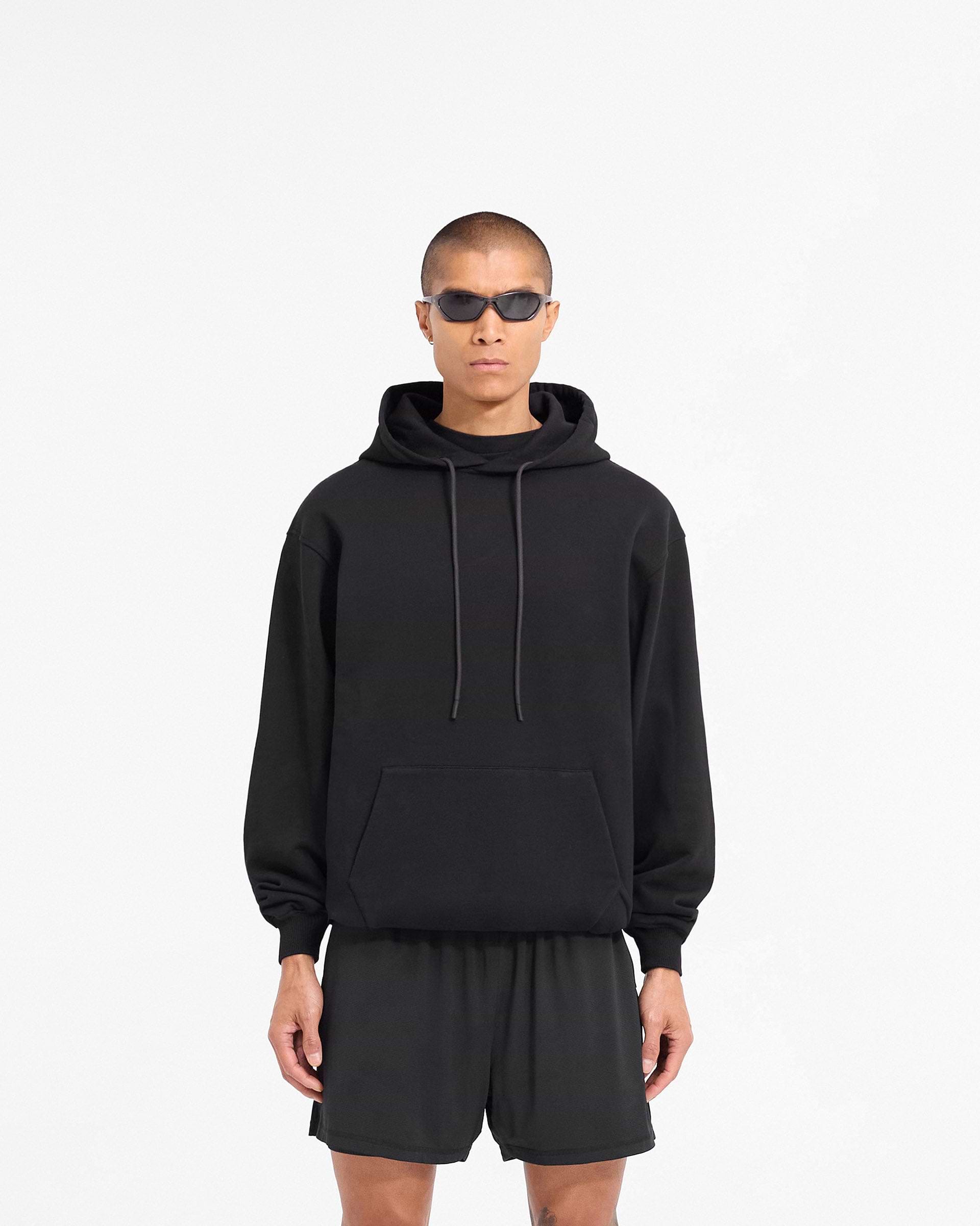 Man wearing a black oversized hoodie on a plain white background | 247 DNA Oversized Hoodie in Black | Oversized hoodie with ribbed cuffs and tonal logo | 247 Hoodies | Represent Clo