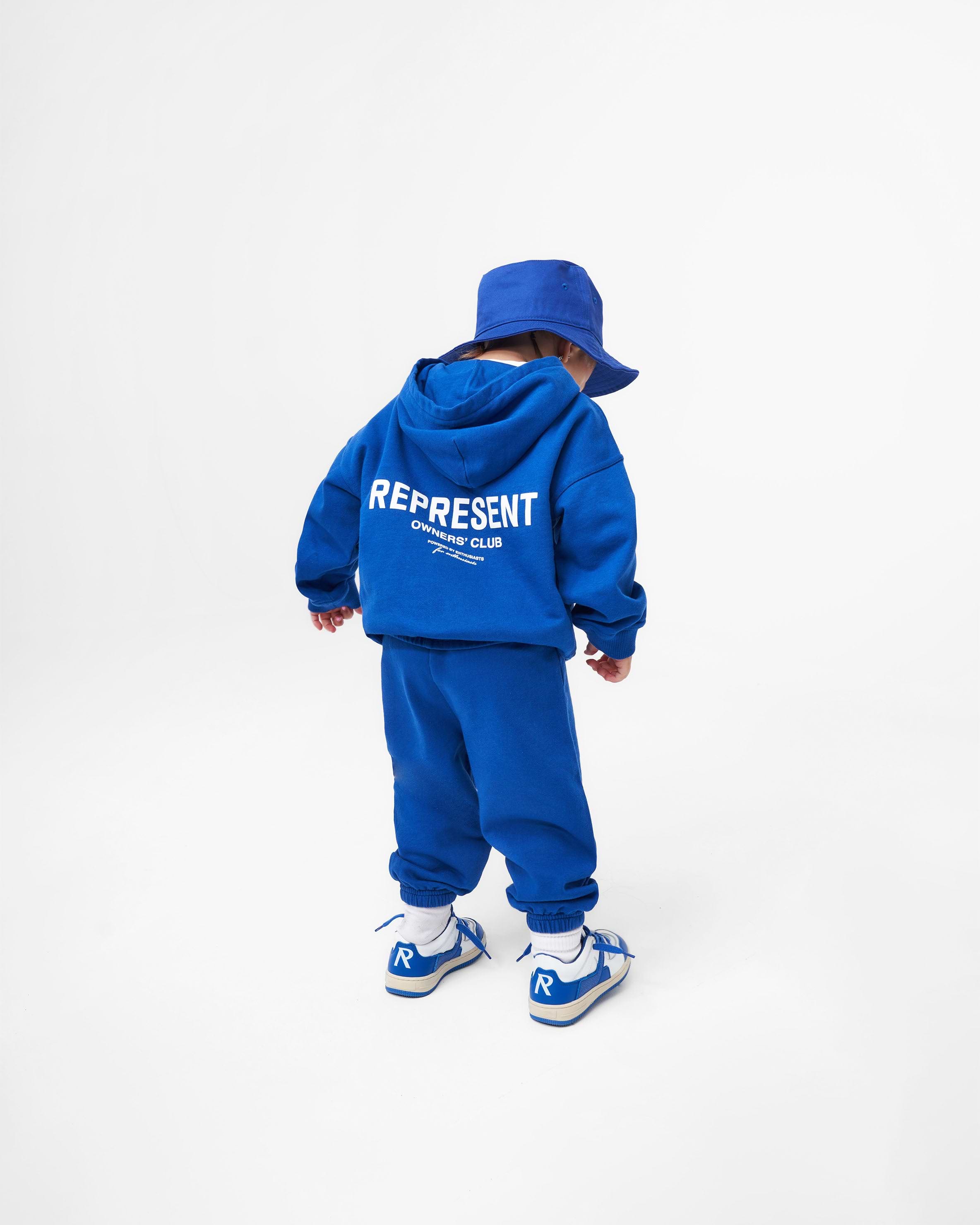 Child wearing a blue hoodie on a plain white background | Represent Mini Owners Club Hoodie in Cobalt | Oversized kids hoodie with screen printed graphic | Owners Club Hoodies | Represent Clo