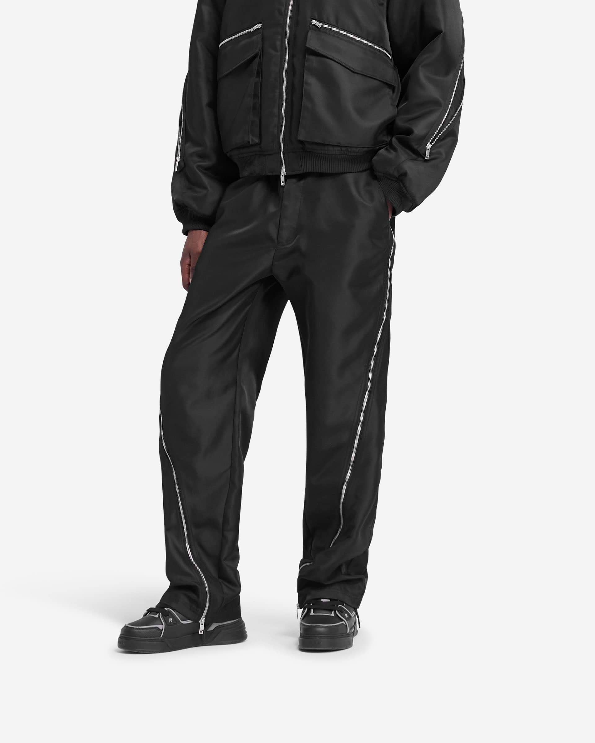 Man wearing black pants on a plain white background | Zip Panel Pant in Jet Black | Shiny nylon twill pants with zip and pockets | FW24 Pants | Represent Clo