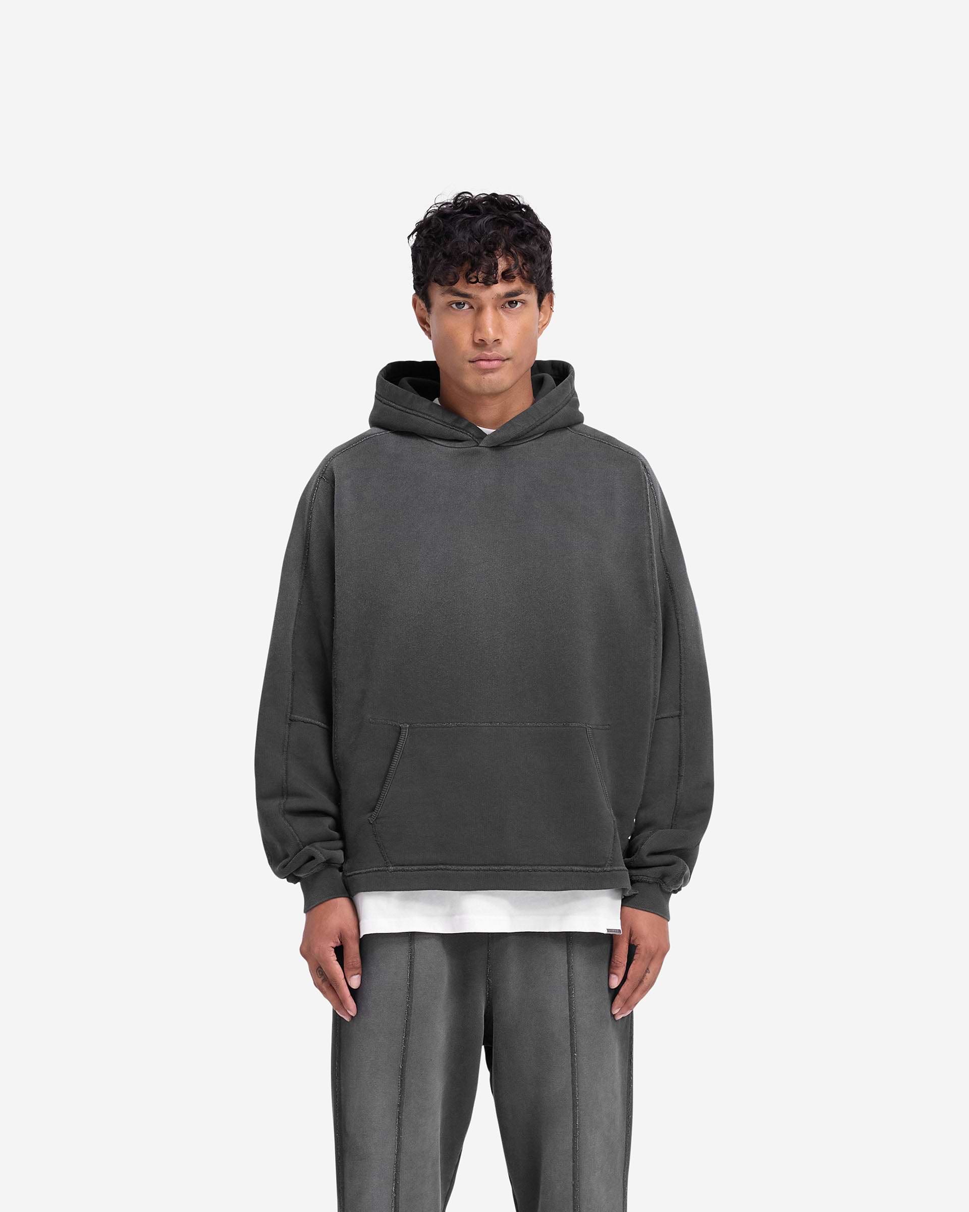 Man wearing an oversized black hoodie on a plain white background | Stepped Hem Hoodie in Stained Black | Split stepped hem and raw edge patch | FW24 Hoodies | Represent Clo
