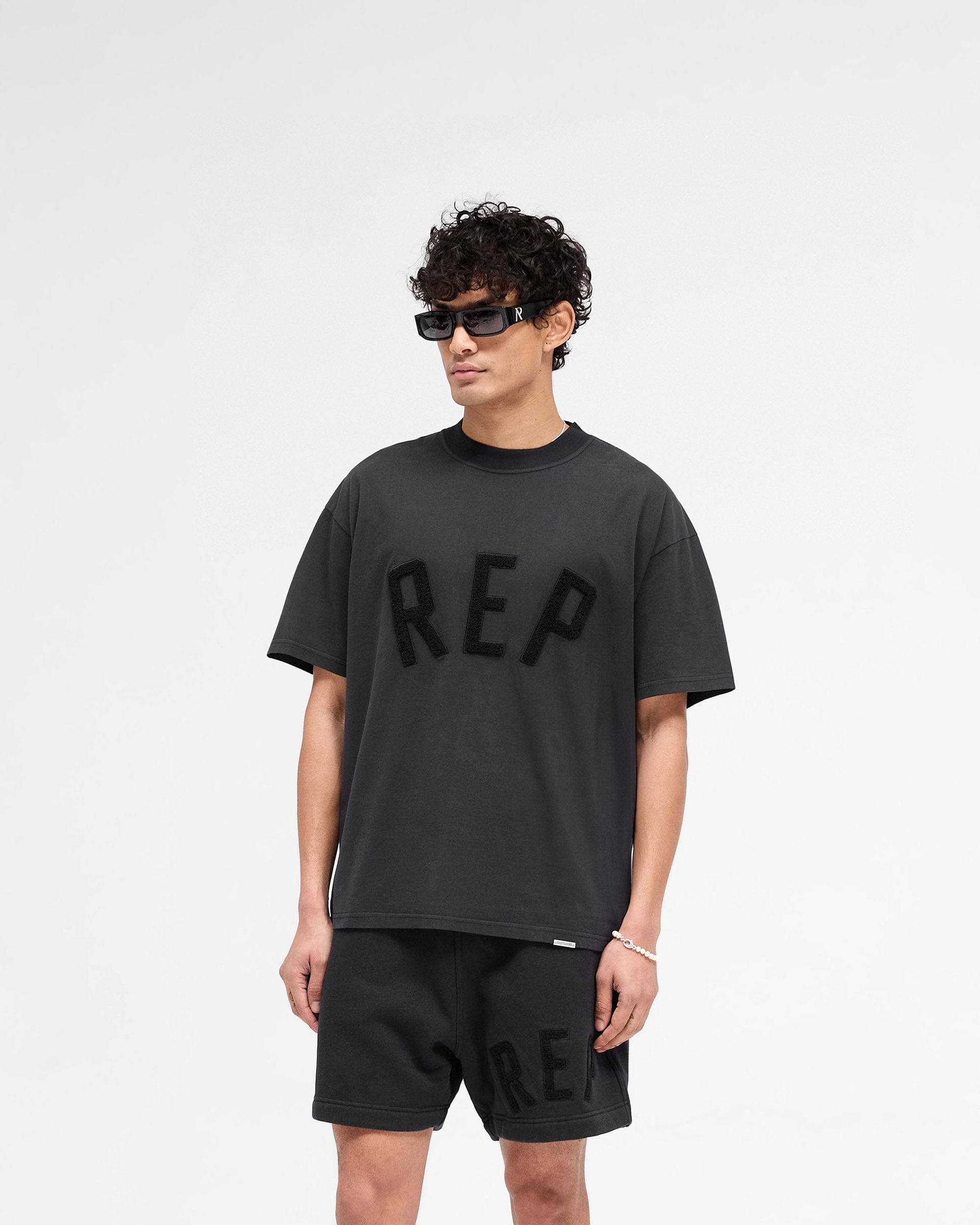 Back product image of a mens black t-shirt on a plain white background | Rep Applique T-Shirt in Off Black | Slightly oversized t-shirt with textured applique | SS25 T-Shirts | Represent Clo