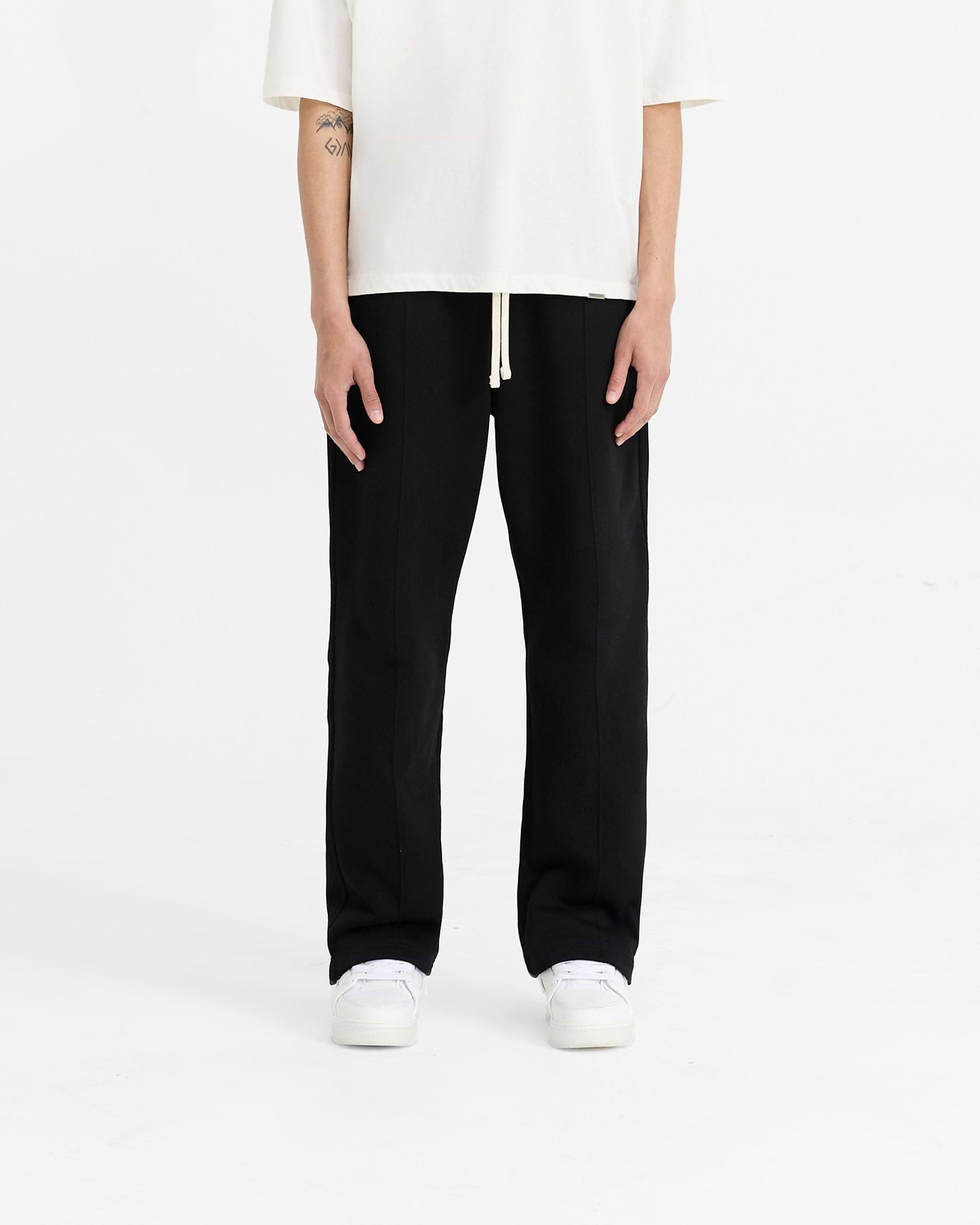 Man wearing black wide leg sweatpants on a plain white background | Initial Sweatpant in Black | Sweatpants with pintuck detail and elasticated waistband | Initial Pants | Represent Clo