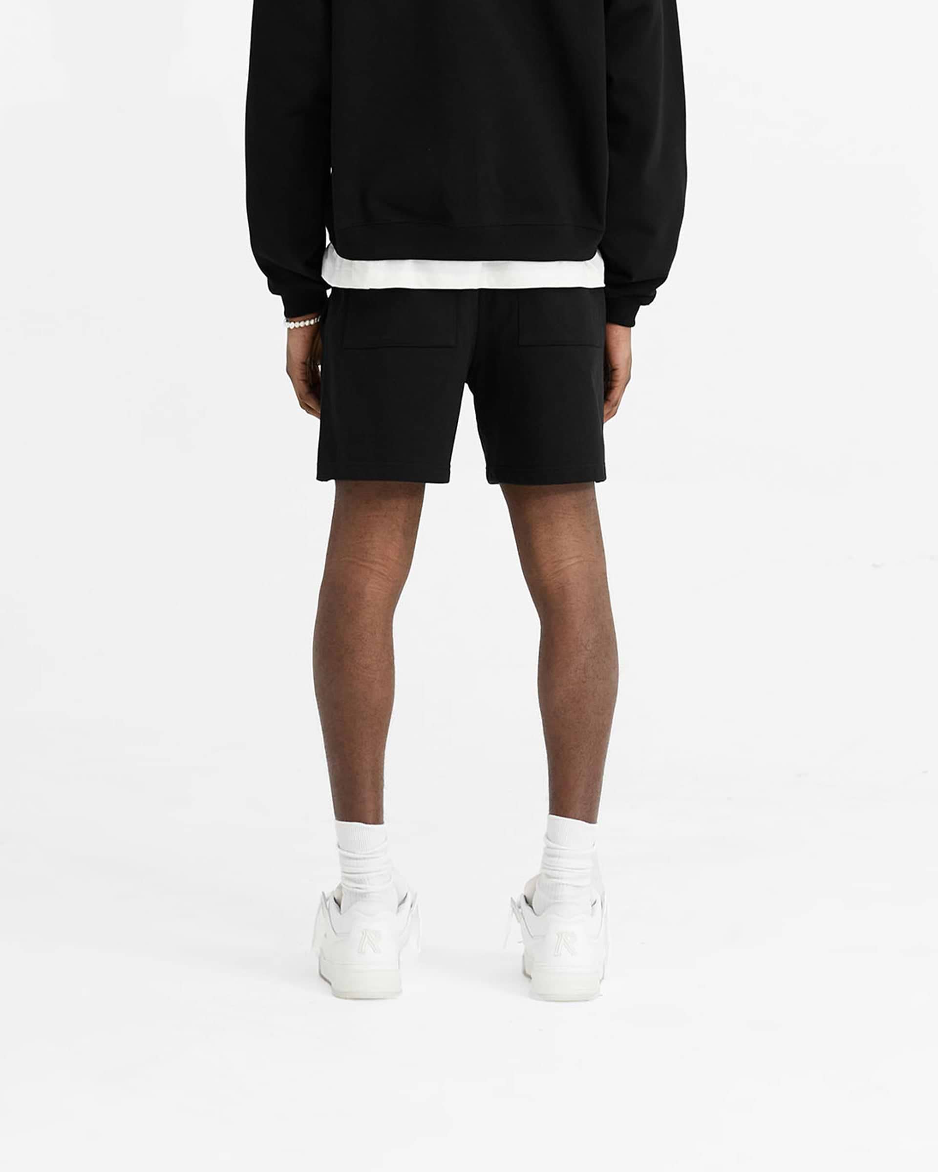 Man wearing black initial sweatshorts on a plain white background | Initial Sweatshorts in Black | Oversized boxy fit sweatshorts with elasticated waistband | Initial Shorts | Represent Clo