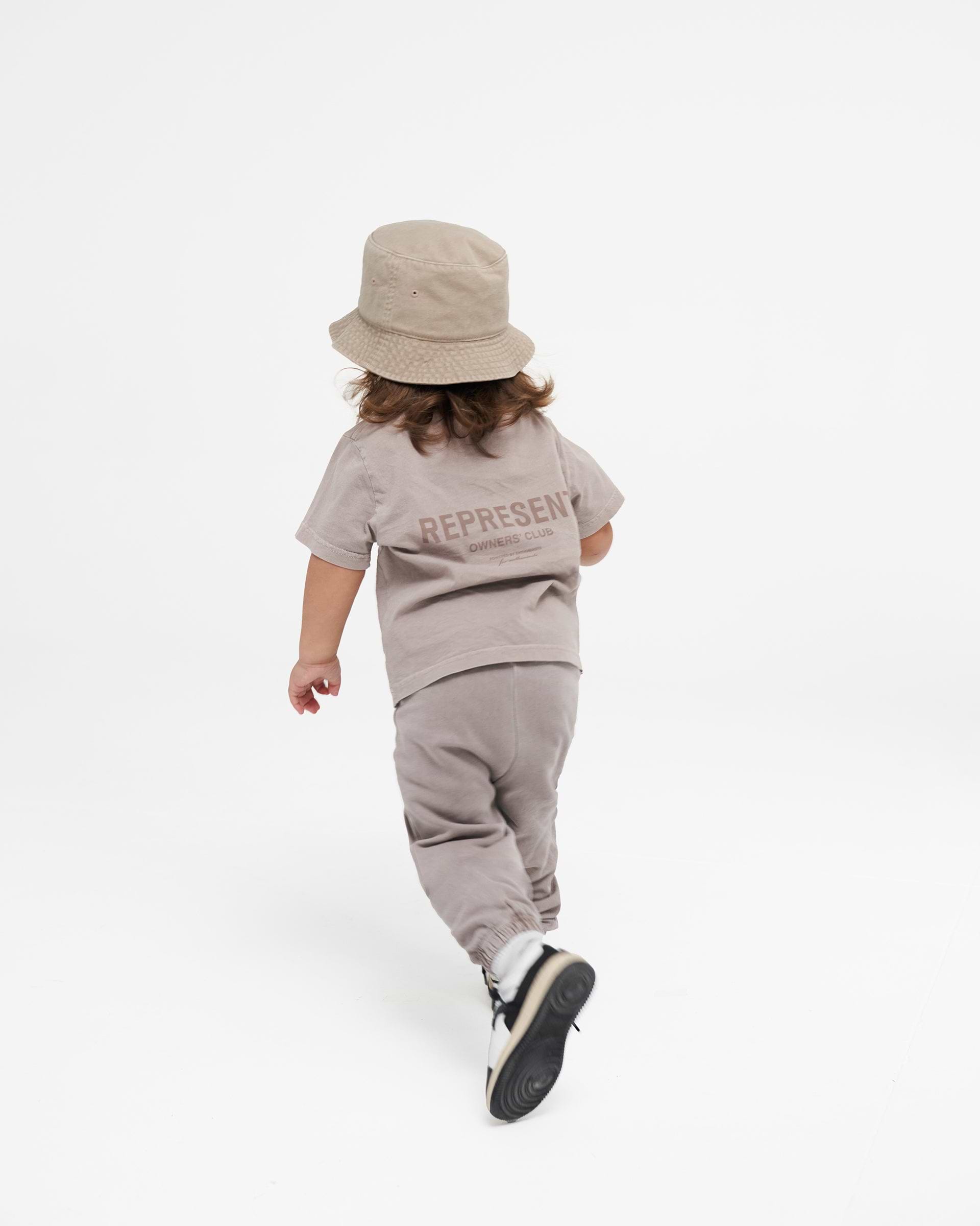 Child wearing mushroom sweatpants on a plain white background | Represent Mini Owners Club Sweatpants in Mushroom | Children's sweatpants with elasticated waistband and cuffs | Owners Club Pants | Represent Clo