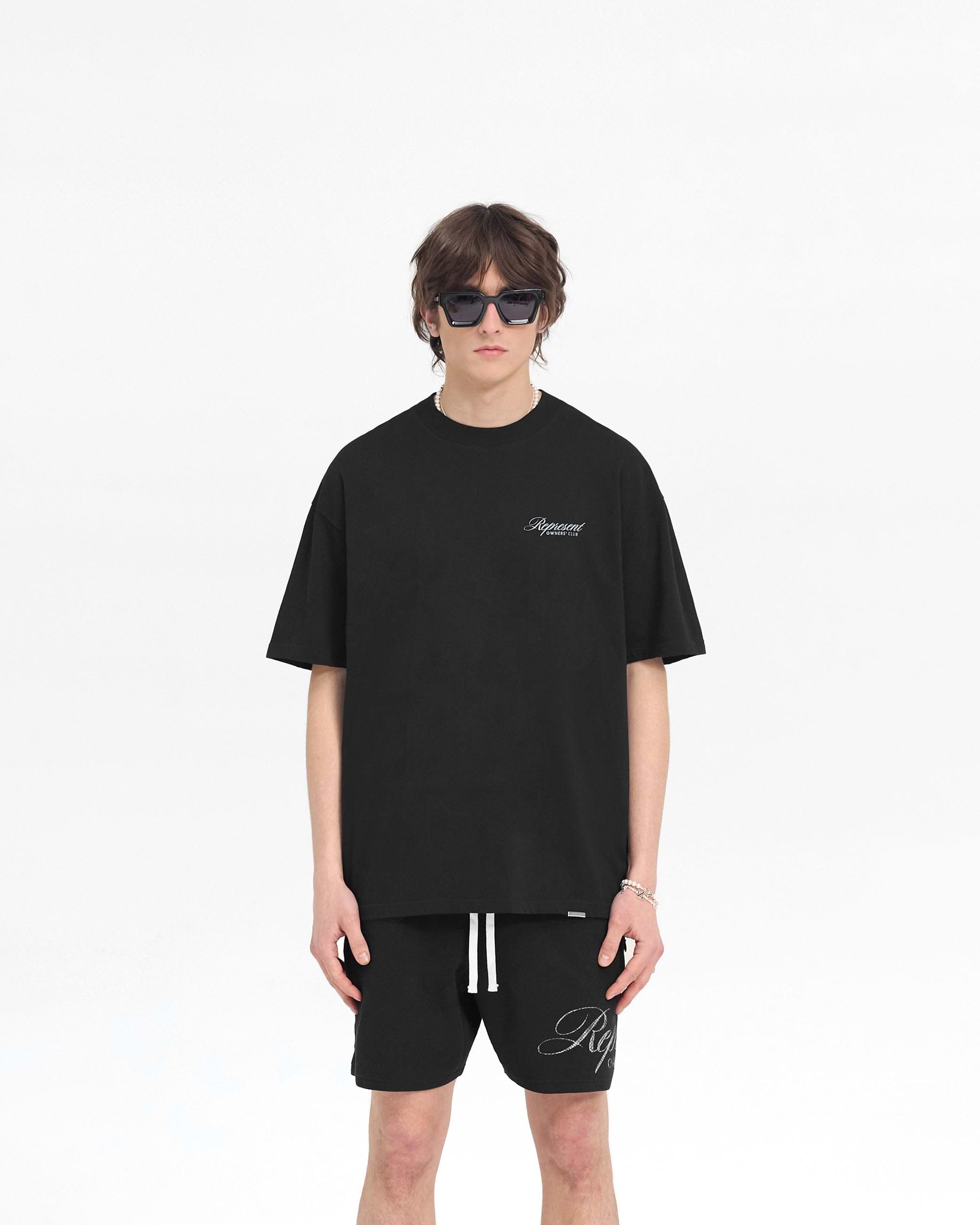 Man wearing an oversized black t-shirt on a plain white background | Represent Owners Club Script T-Shirt in Black | Overized t-shirt with a script graphic and round neck | Owners Club T-Shirts | Represent Clo