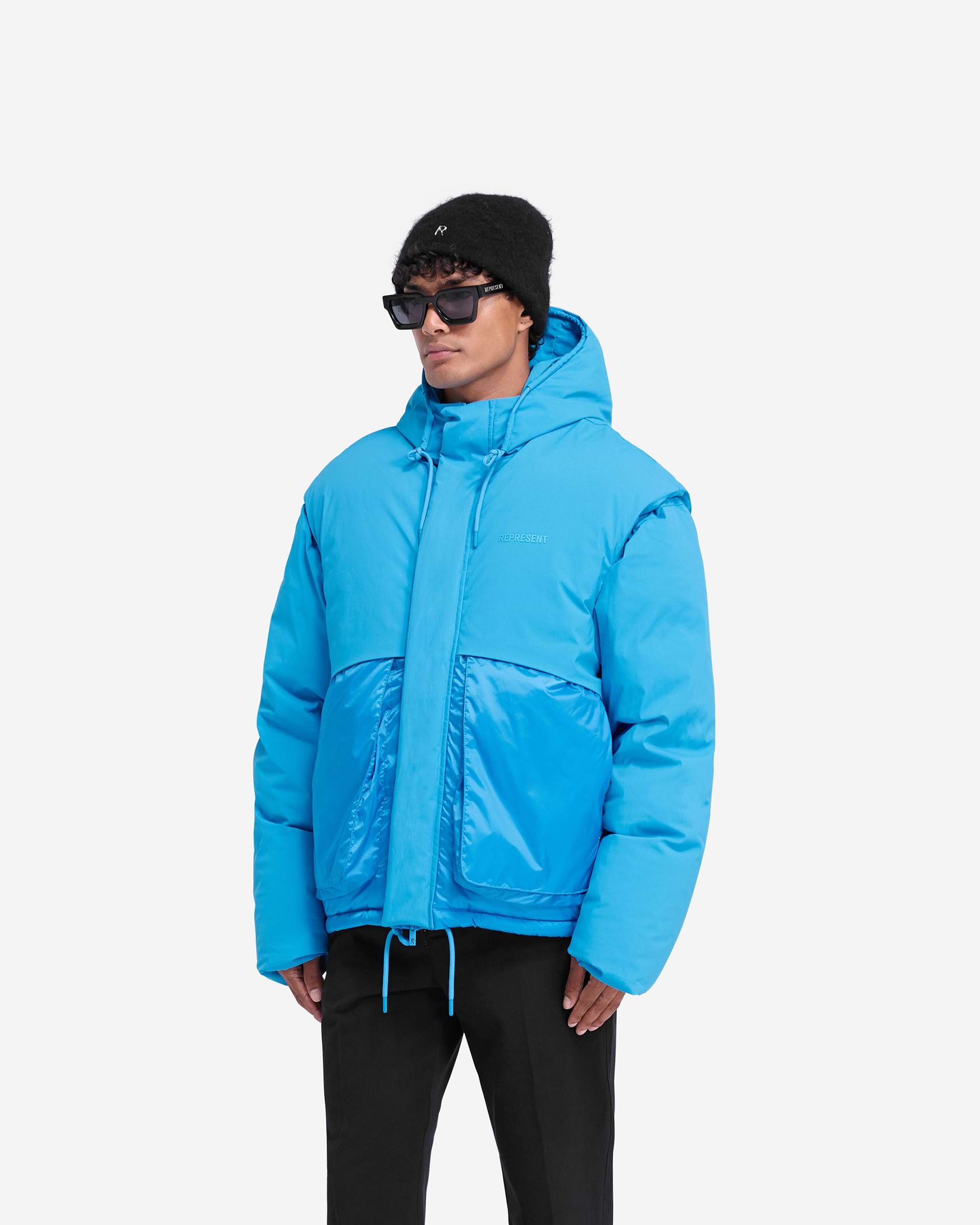 Back product image of a mens blue puffer jacket on a plain white background | Layered Hooded Puffer in Electric Blue | Duck down filled jacket with storm flaps and tonal branding | FW24 Outerwear | Represent Clo