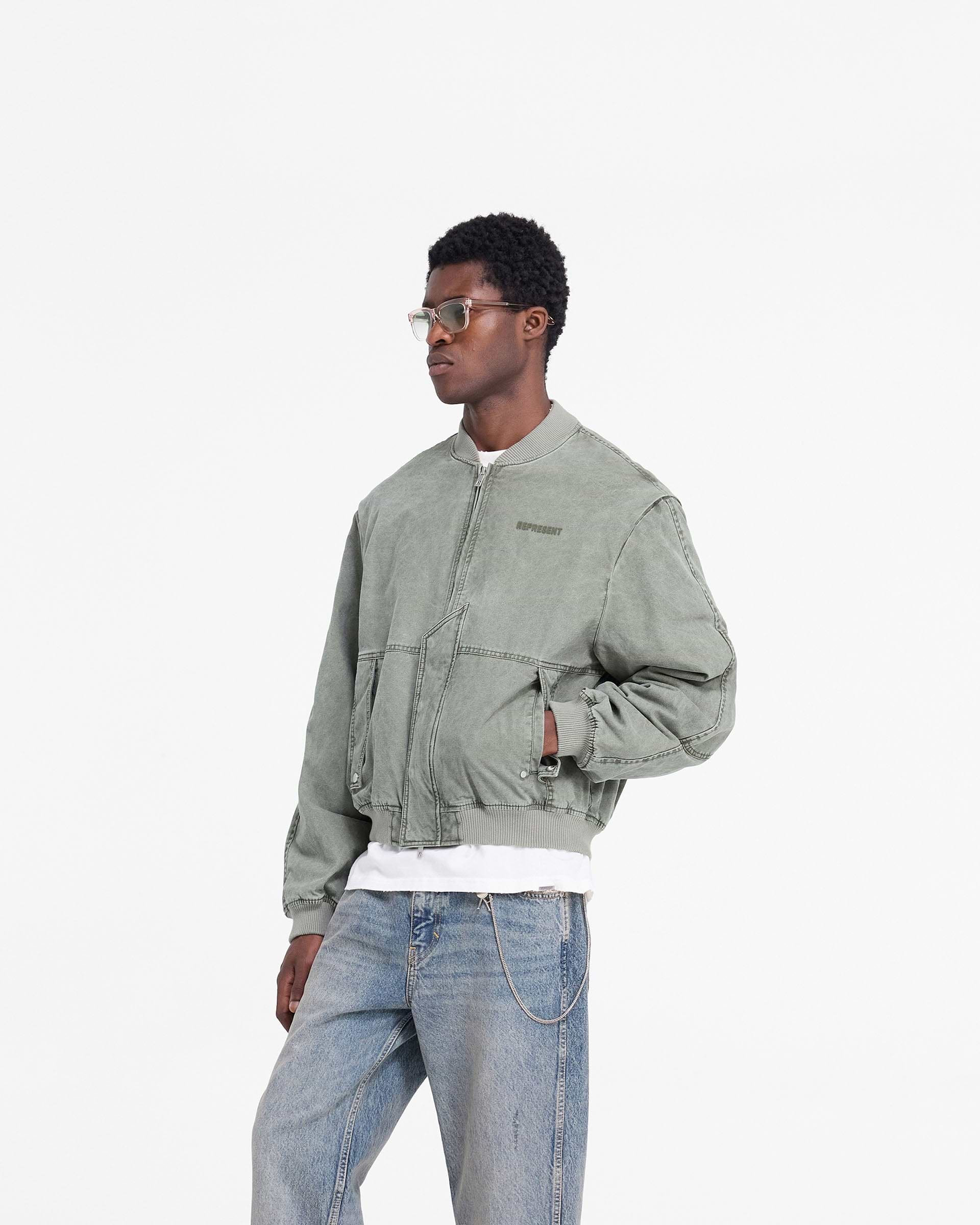 Man wearing a khaki bomber jacket on a plain white background | Inset Sleeve Bomber in Khaki | Cotton bomber jacket with asymmetric placket and zip guard | FW24 Outerwear | Represent Clo