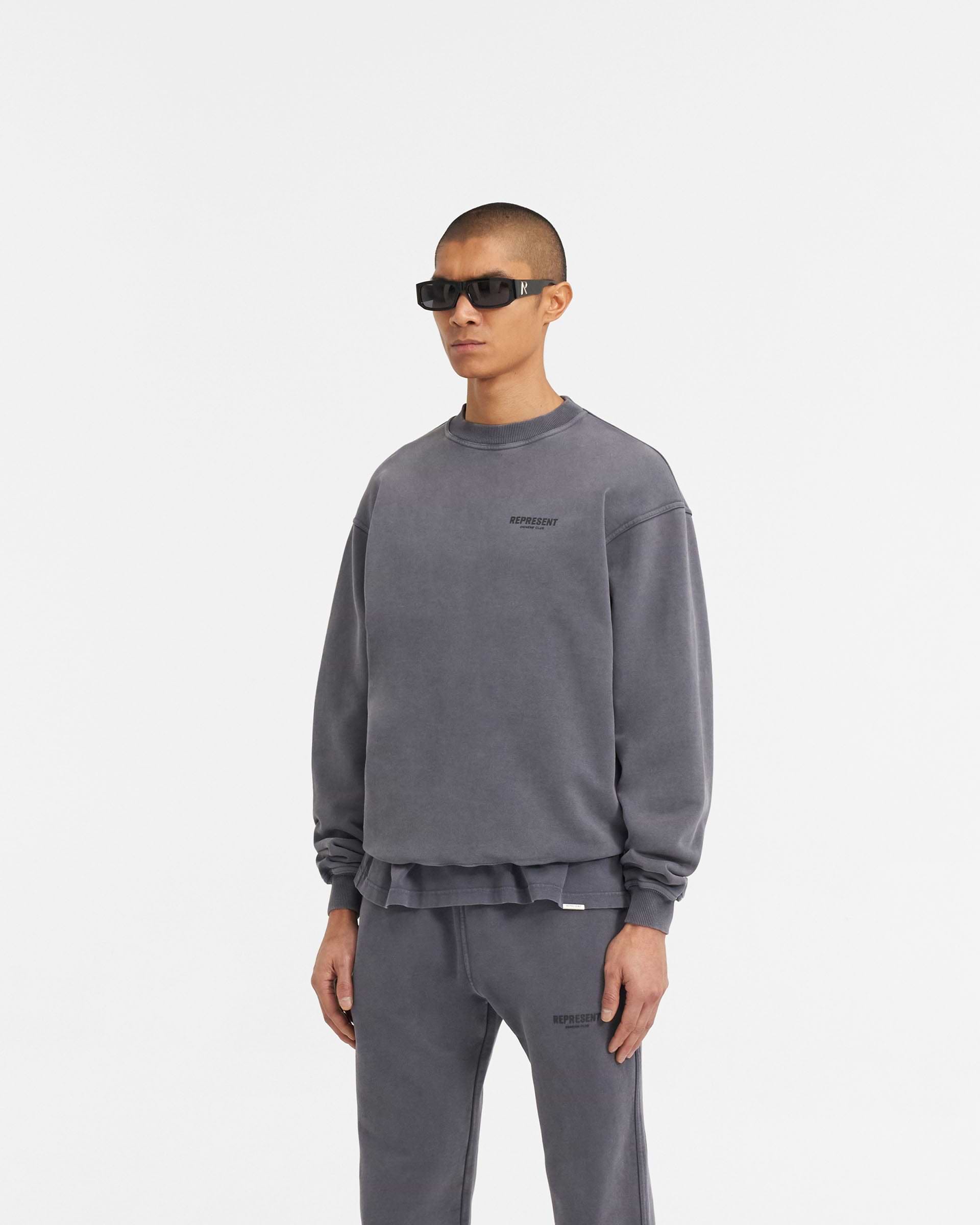 Man wearing a grey oversized sweater on a plain white background | Represent Owners Club Sweater in Storm | Heavyweight jersey cotton crewneck sweater with high build branding | Owners Club Sweaters | Represent Clo