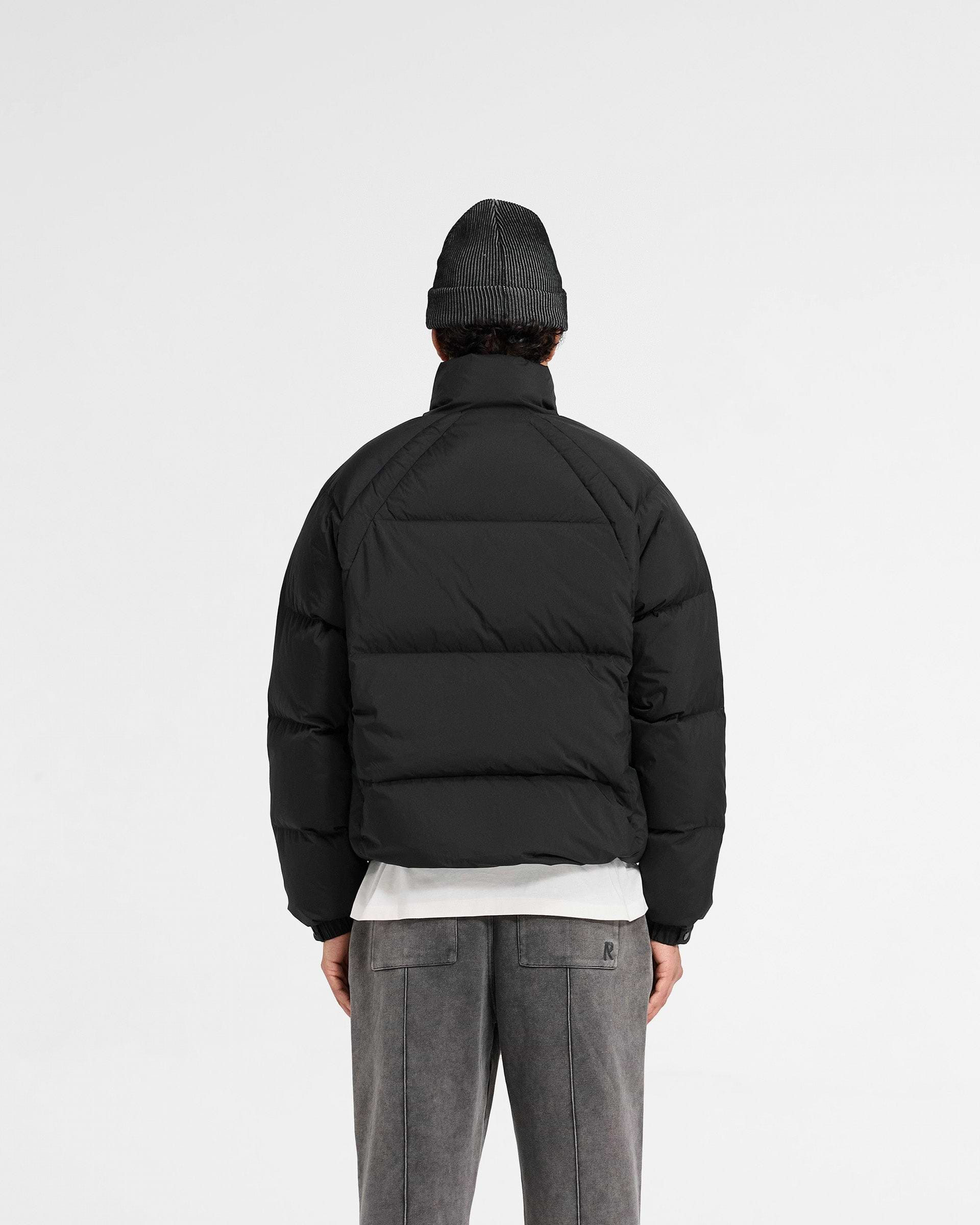 Man wearing a black puffer jacket on a plain white background | Funnel Neck Puffer in Black | Puffer jacket with raglan sleeves and toggle hem adjustment | PRE SS25 Outerwear | Represent Clo