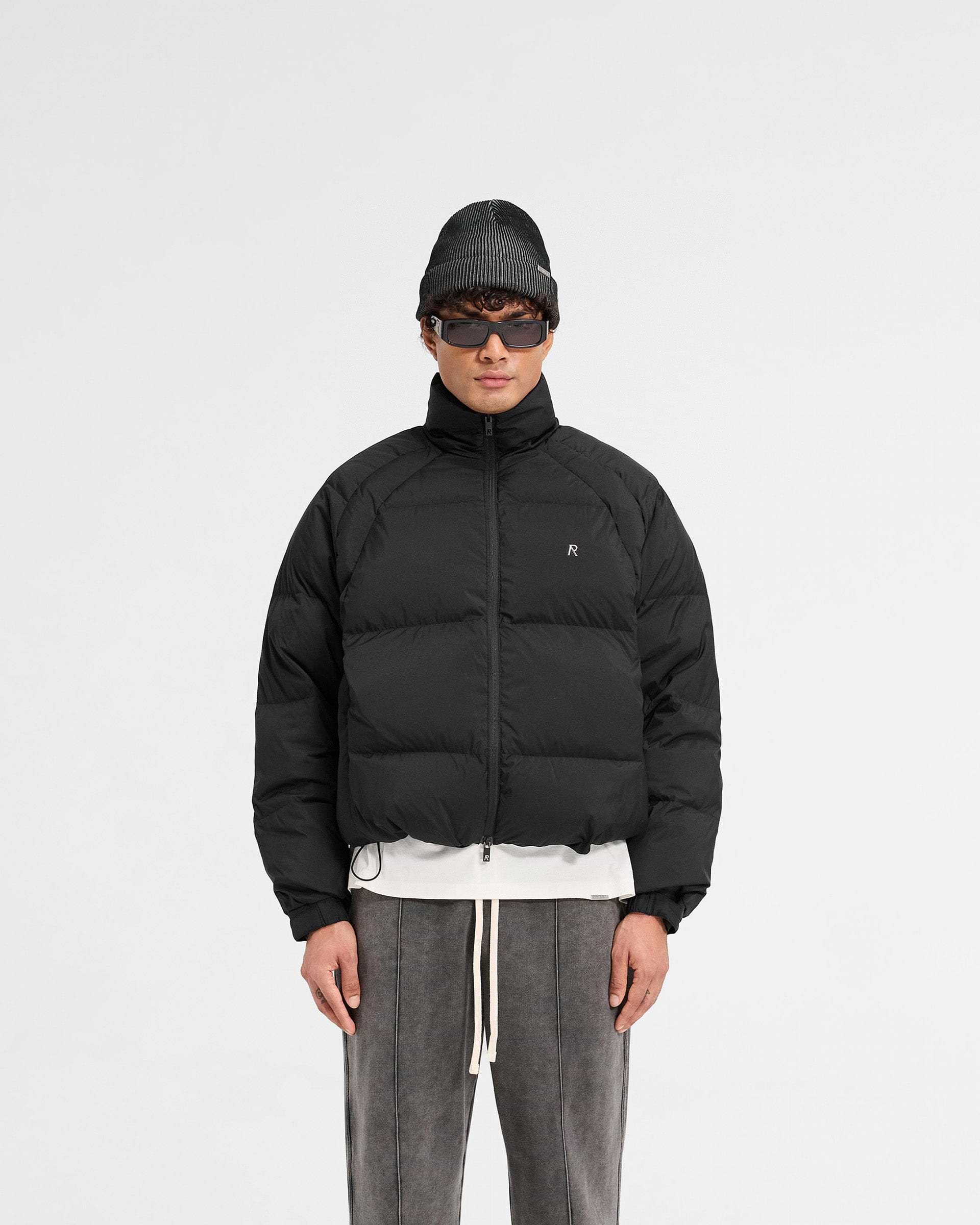 Man wearing a black puffer jacket on a plain white background | Funnel Neck Puffer in Black | Puffer jacket with raglan sleeves and micro fleece lined pockets | PRE SS25 Outerwear | Represent Clo