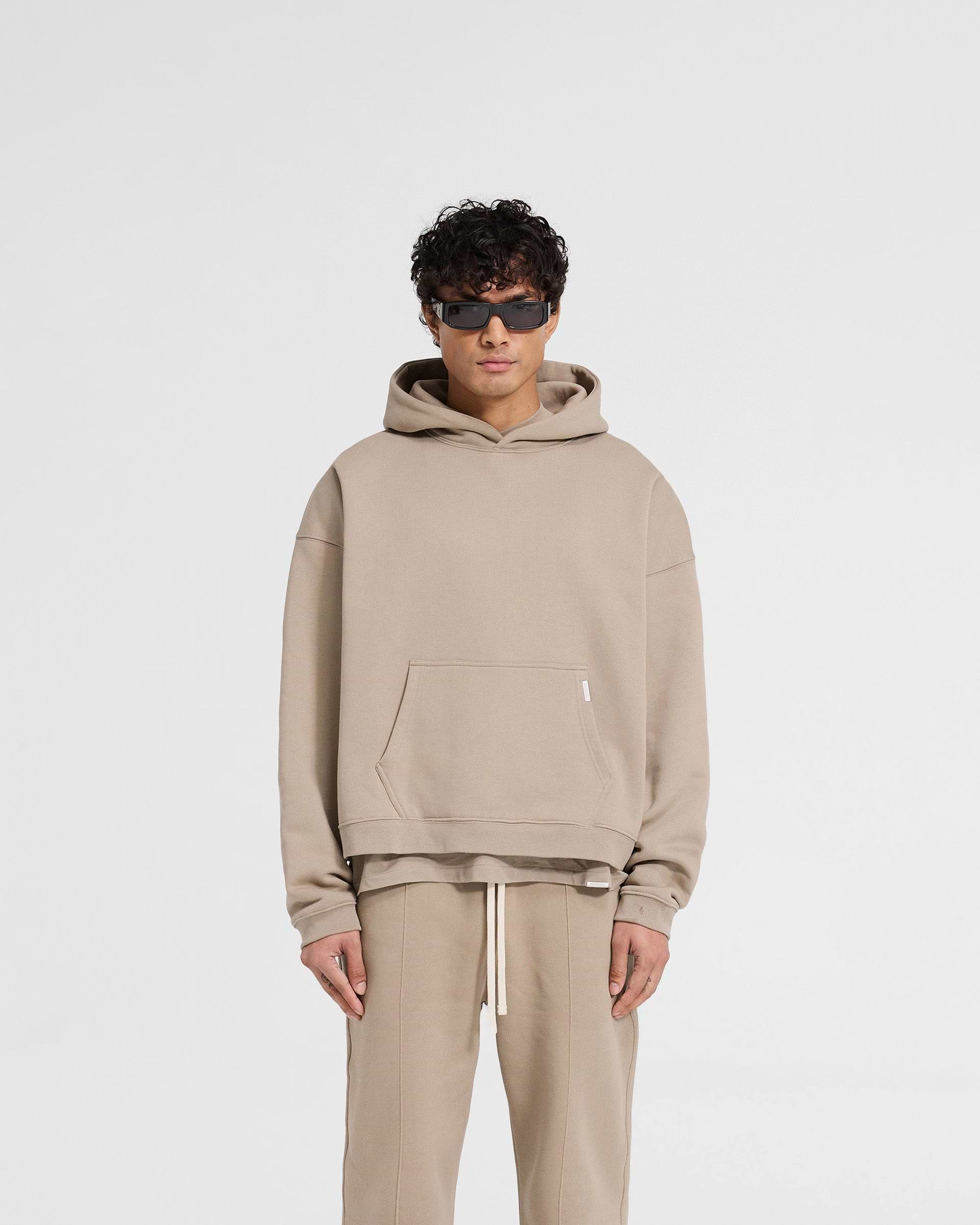 Man wearing an oversized beige hoodie on a plain white background | Initial Boxy Hoodie in Dune | Boxy fit oversized hoodie with dropped shoulders | Initial Hoodies | Represent Clo