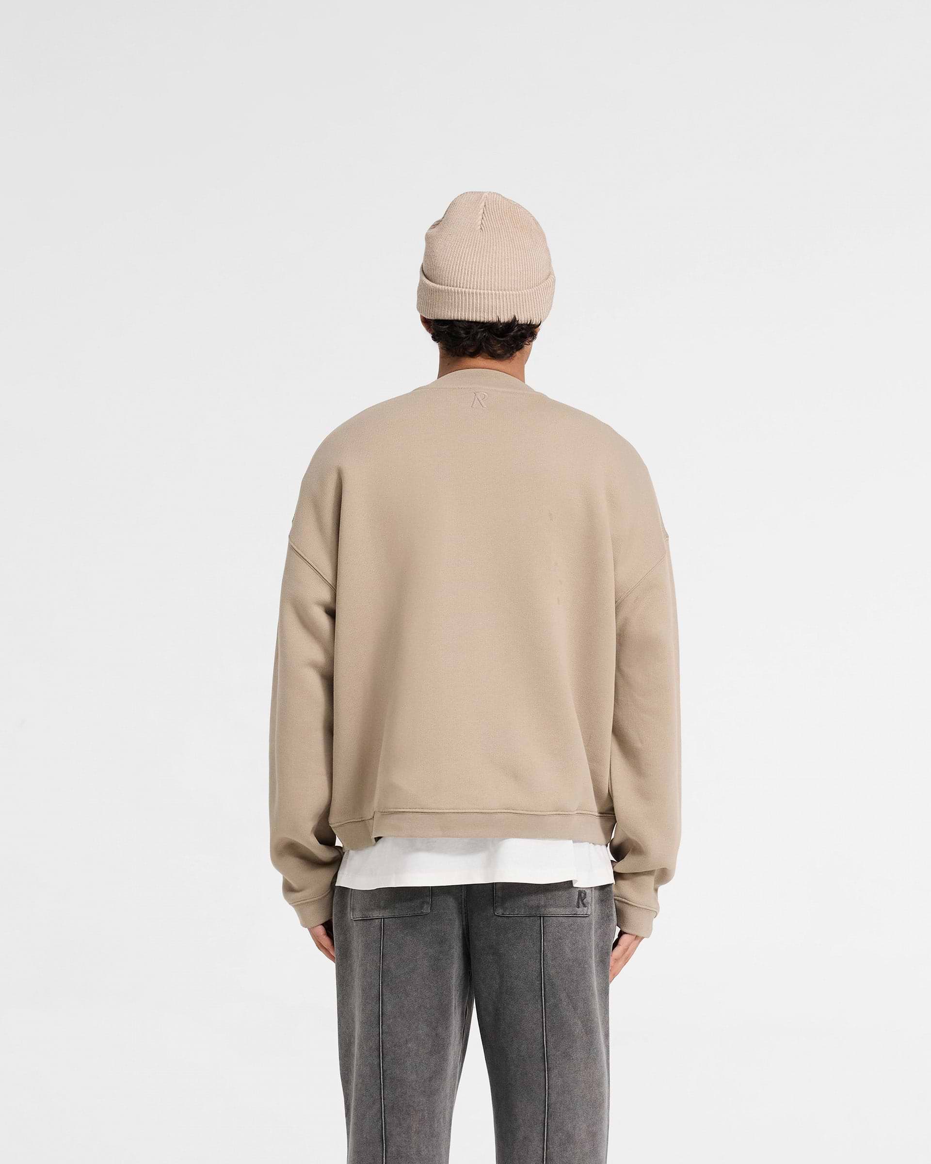 Man wearing an oversized beige sweater on a plain white background | Initial Boxy Sweater in Dune | Boxy fit sweater with super cropped body | Initial Sweaters | Represent Clo