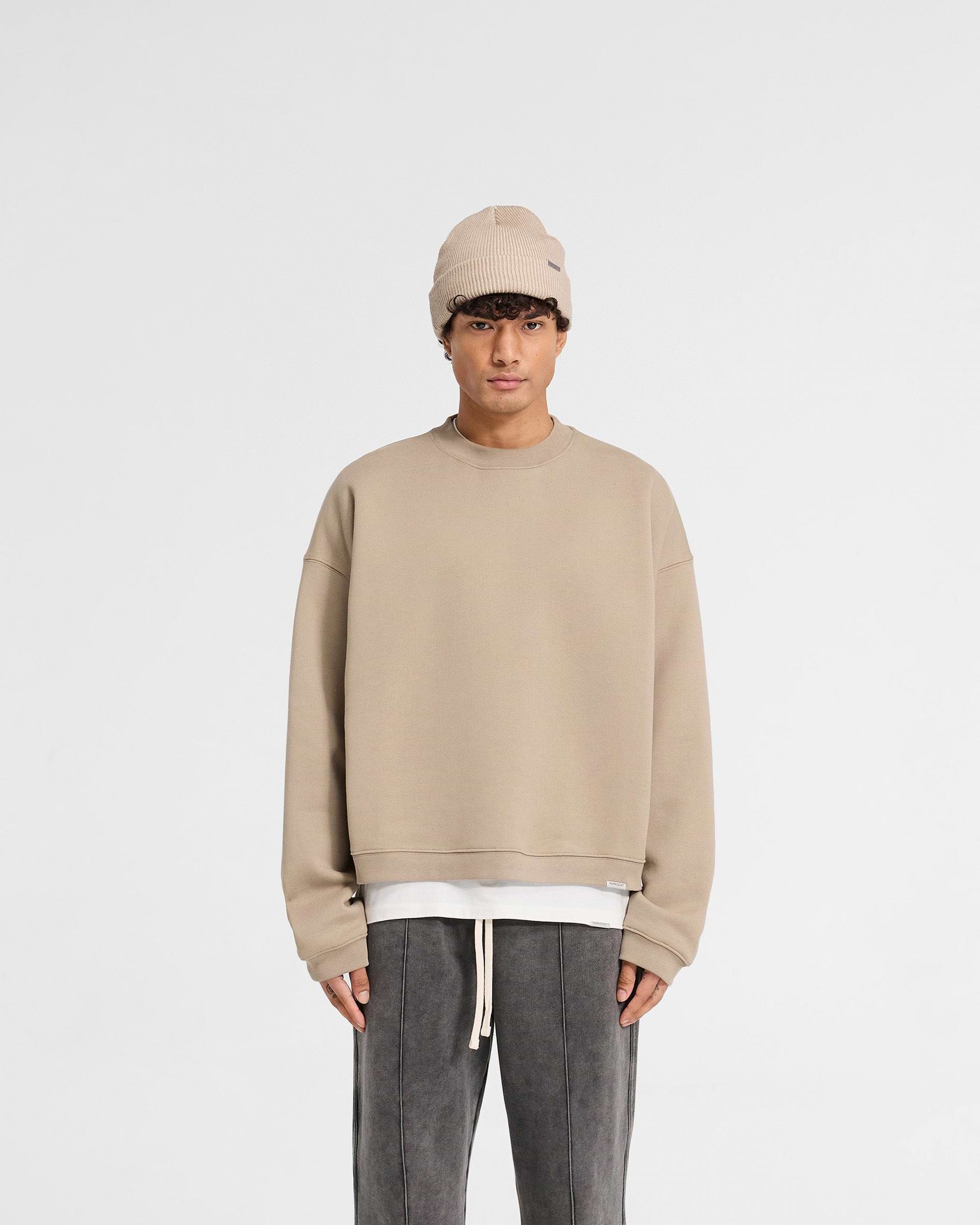 Man wearing a beige oversized sweater on a plain white background | Initial Boxy Sweater in Dune | Boxy fit sweater with dropped shoulders | Initial Sweaters | Represent Clo