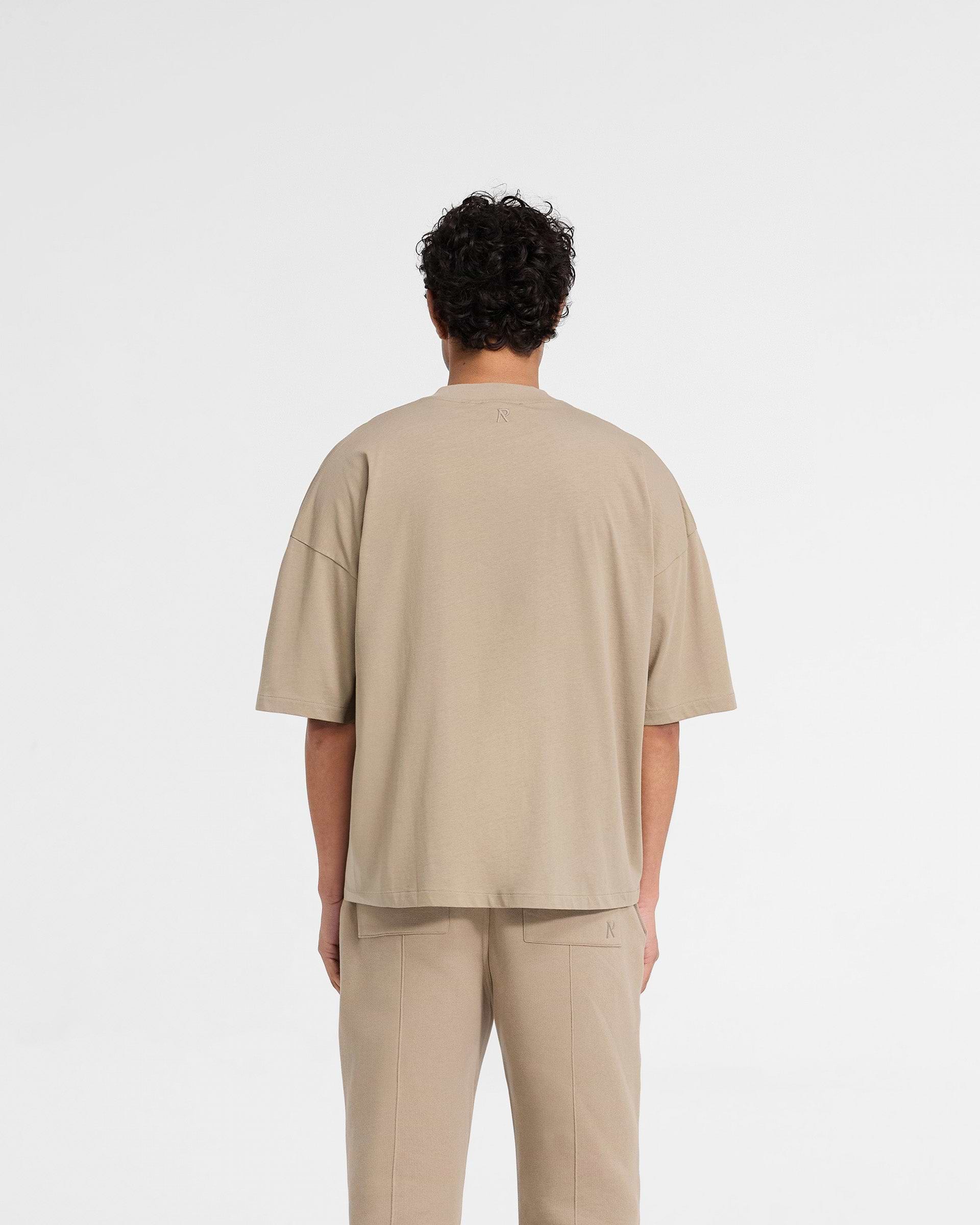 Man wearing an oversized dune t-shirt on a plain white background | Initial Boxy T-Shirt in Dune | Boxy cropped t-shirt with ribbed collar | Initial T-Shirts | Represent Clo