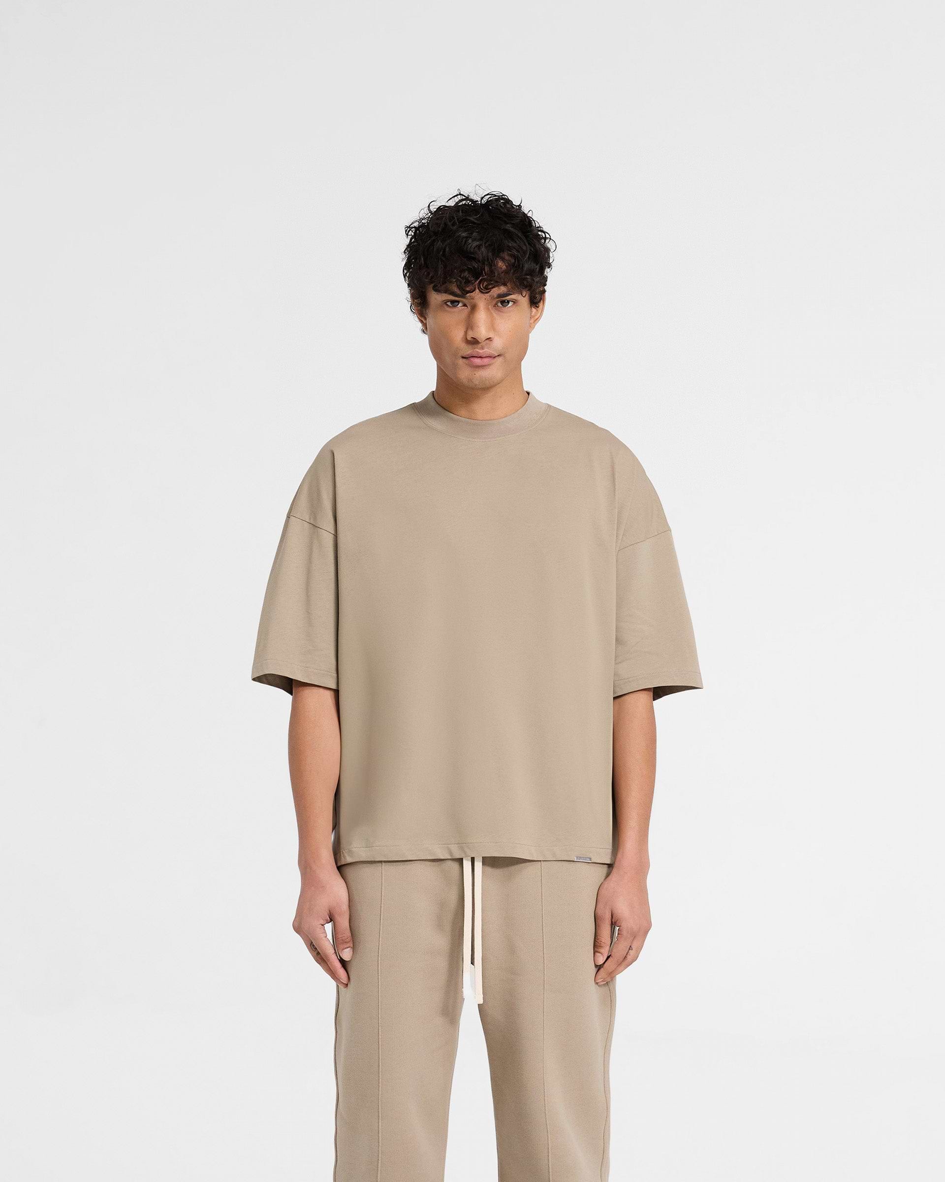 Man wearing an oversized dune t-shirt on a plain white background | Initial Boxy T-Shirt in Dune | Oversized and boxy cropped t-shirt in heavy cotton | Initial T-Shirts | Represent Clo