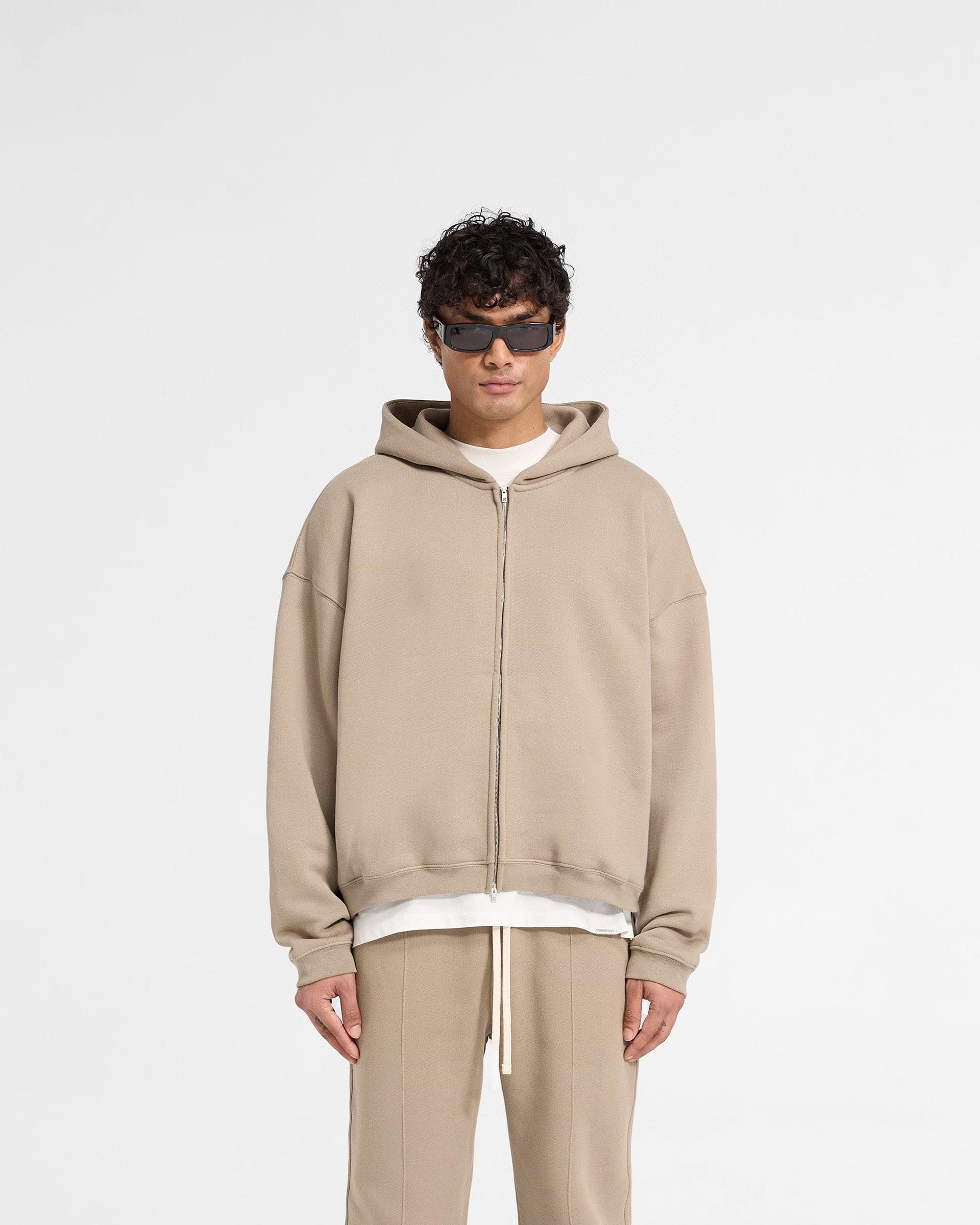 Man wearing an oversized beige hoodie on a plain white background | Initial Boxy Zip Through Hoodie in Dune | Boxy fit hoodie with front zip and welt pockets | Initial Hoodies | Represent Clo