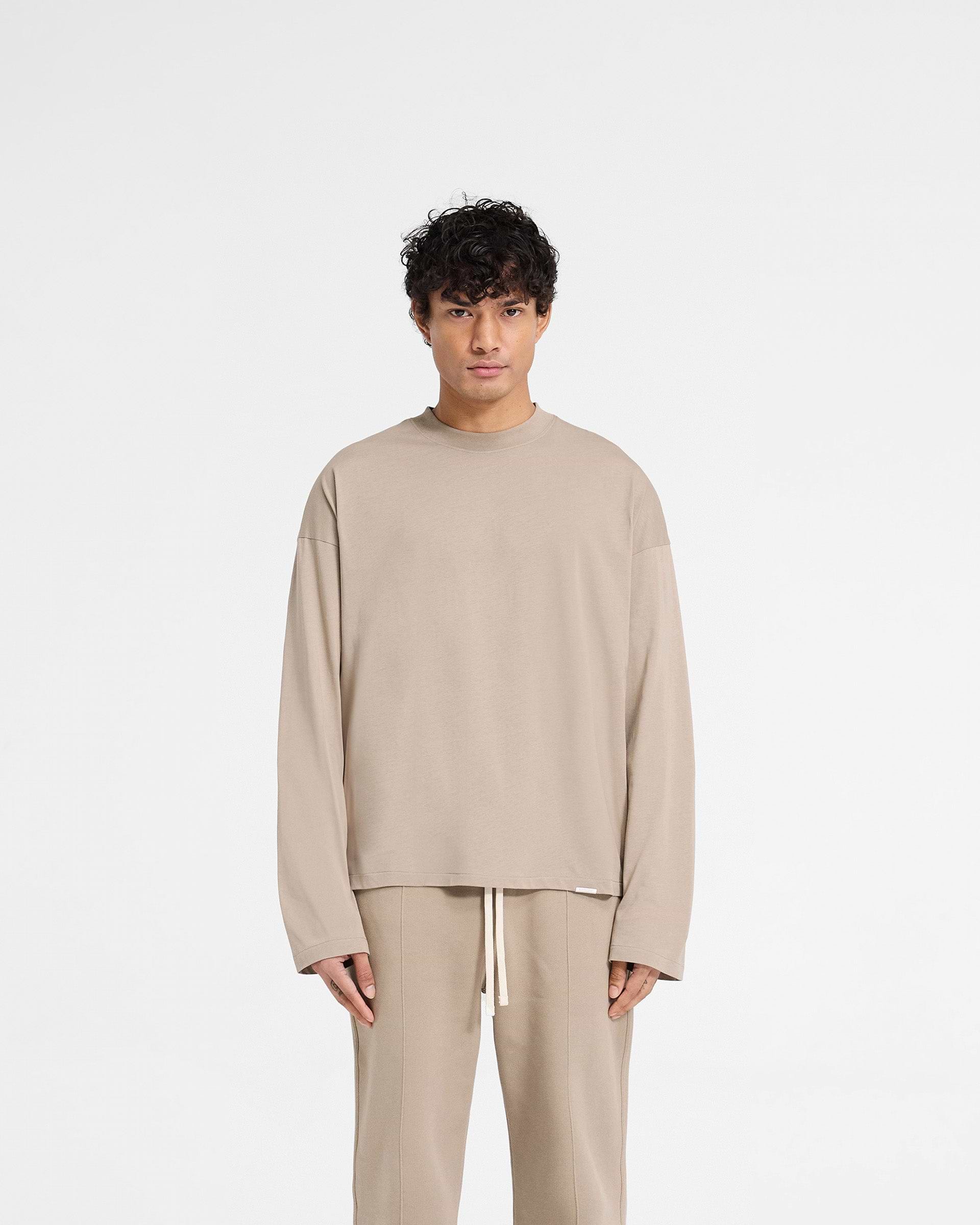 Man wearing a beige t-shirt on a plain white background | Initial Long Sleeve Open Cuff T-Shirt in Dune | Boxy oversized long sleeve t-shirt | Initial T-Shirts | Represent Clo
