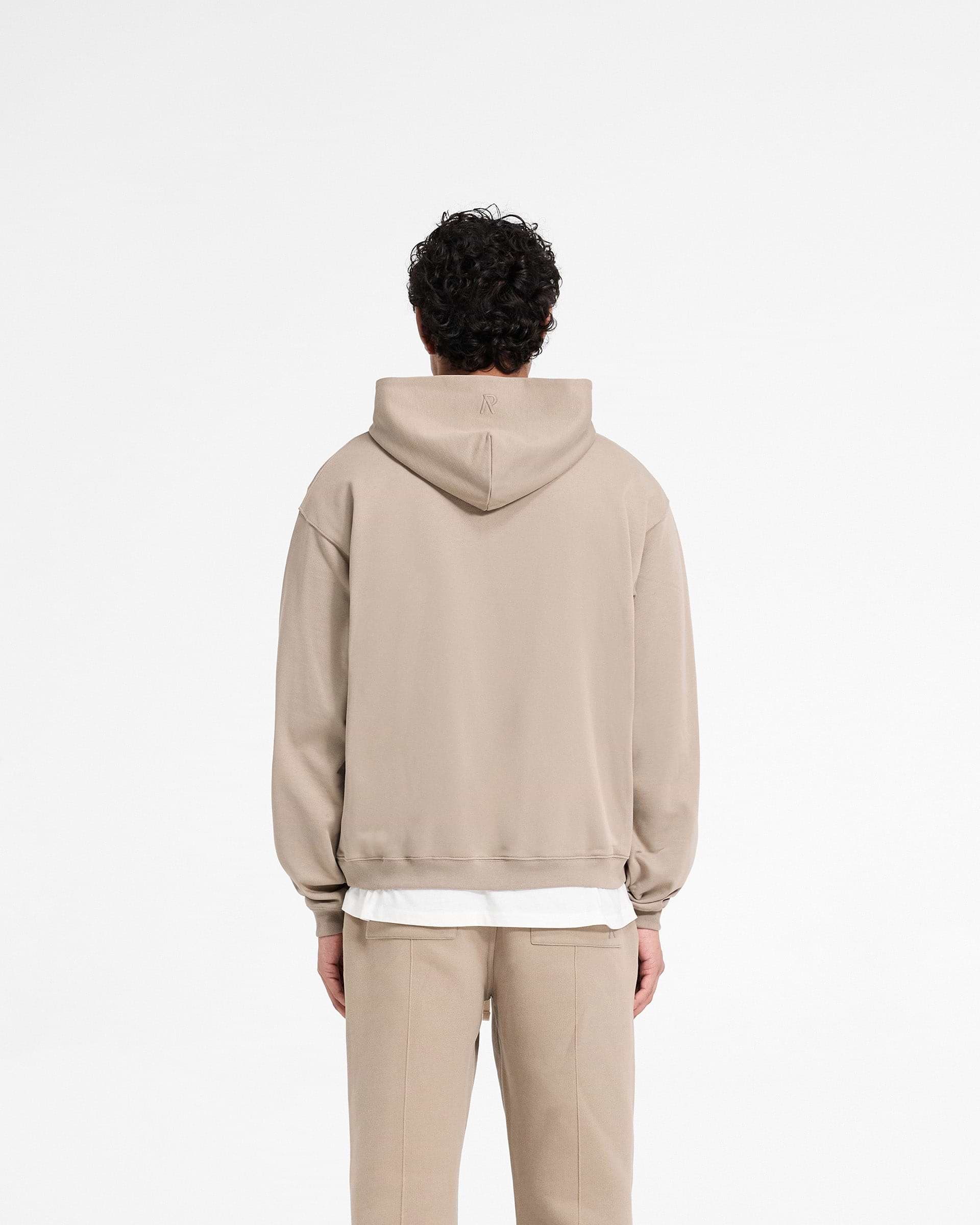 Man wearing an oversized beige zip hoodie on a plain white background | Initial Zip Hoodie in Dune | Oversized zip hoodie with 1x1 rib and side seam pockets | Initial Hoodies | Represent Clo