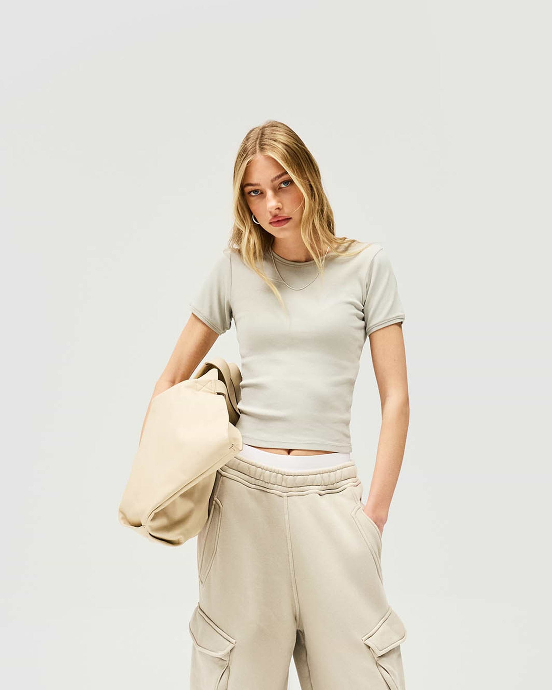 Woman wearing a grey ribbed t-shirt on a plain white background | Initial Rib Baby T-Shirt in Storm | Cropped waist-length fit top | Womens Initial Tops | Represent Clo
