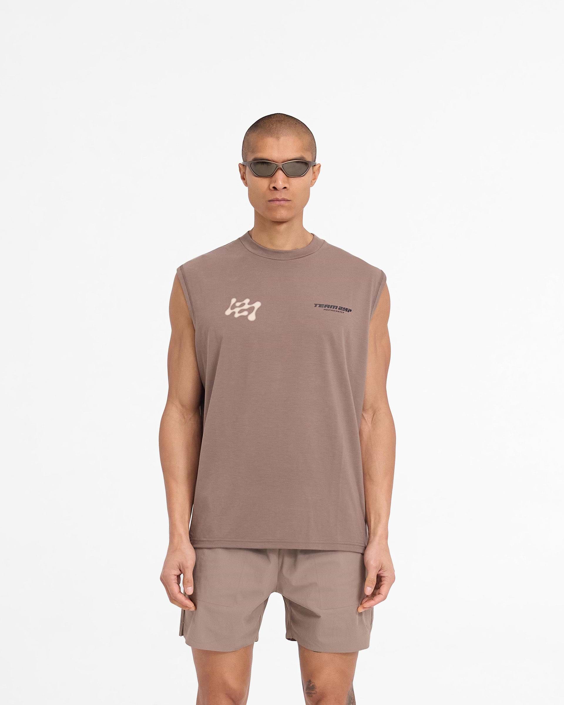 Man wearing an oversized brown tank top on a plain white background | 247 Future Terrains Oversized Tank in Umber | Quick drying training tank | 247 T-Shirts | Represent Clo
