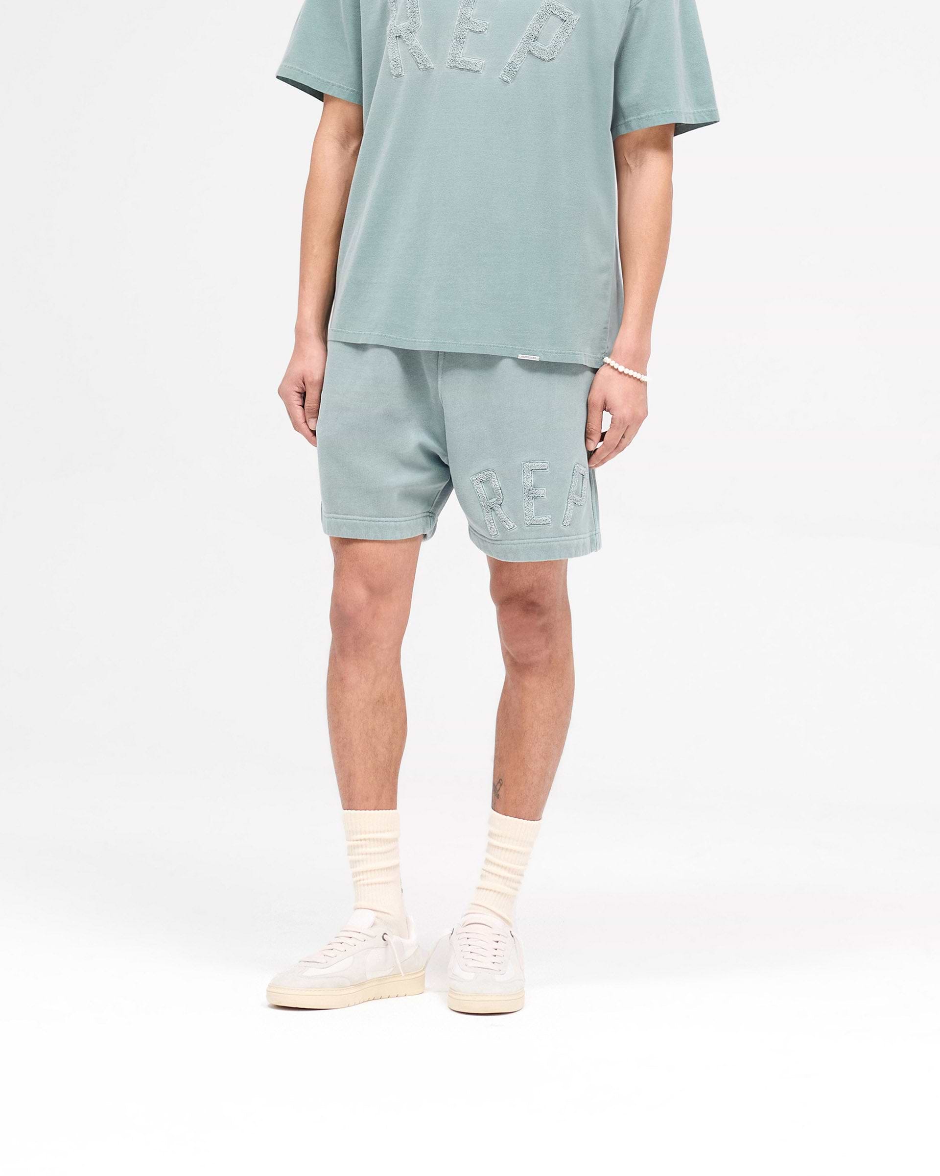 Back product image of mens green shorts on a plain white background | Rep Applique Shorts in Forest Green | Boxy fit shorts with back pockets and applique logo | SS25 Shorts | Represent Clo