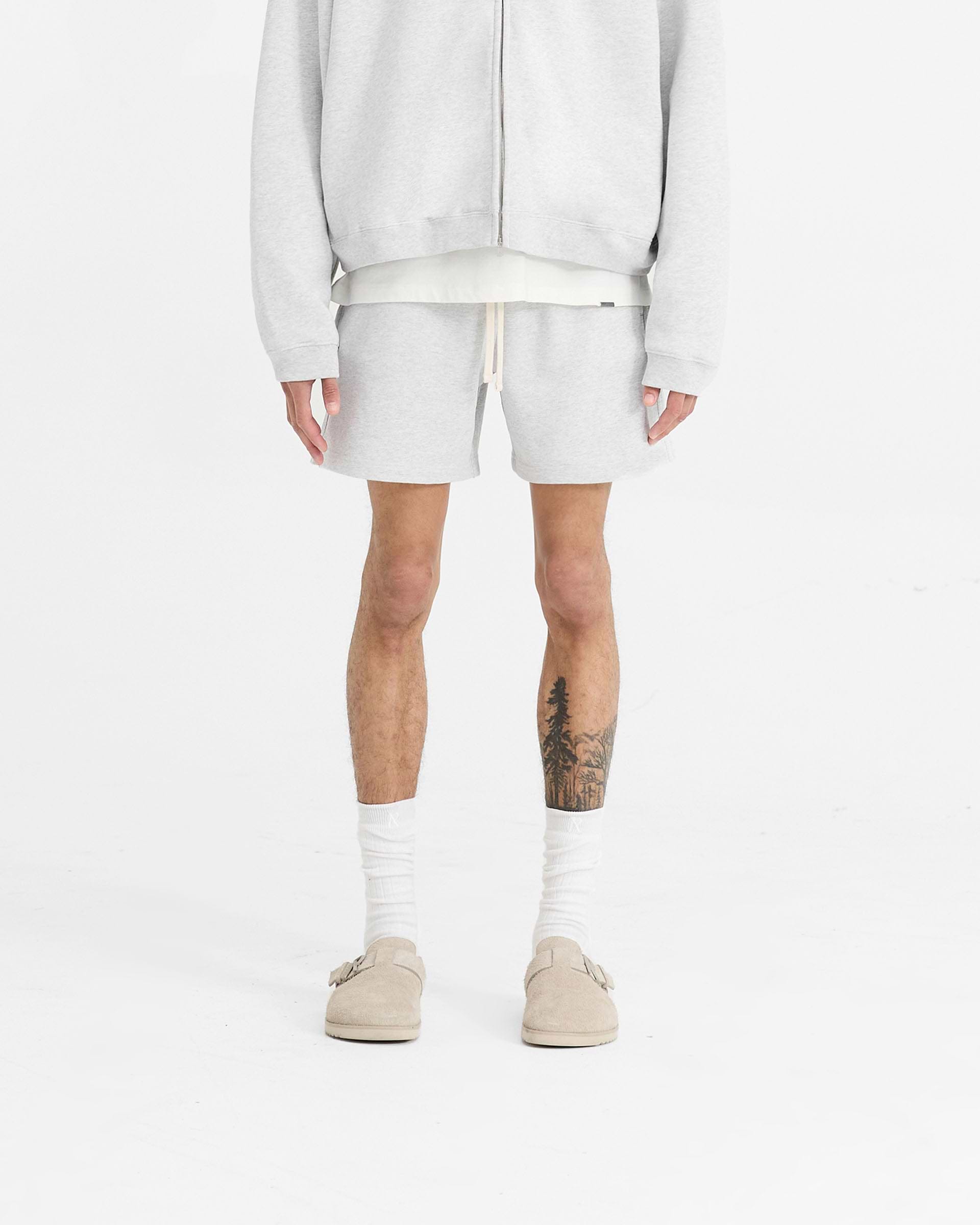 Man wearing grey sweatshorts on a plain white background | Initial Sweatshorts in Ice Grey Marl | Oversized boxy fit shorts with elasticated waistband | Initial Shorts | Represent Clo