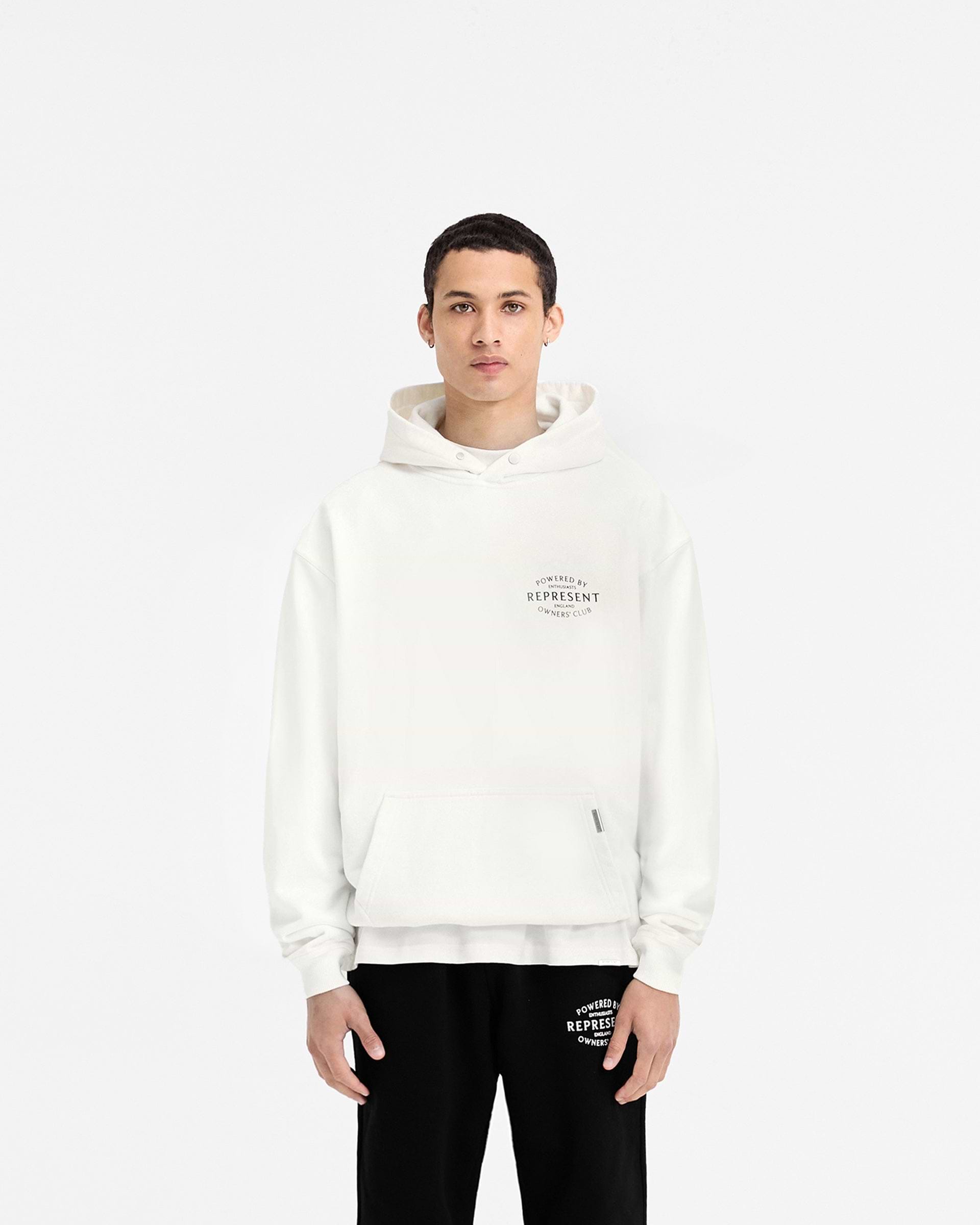 Man wearing a white hoodie on a plain white background | Represent Owners Club Stamp Hoodie in Flat White | Oversized hoodie with branding | Owners Club Hoodies | Represent Clo