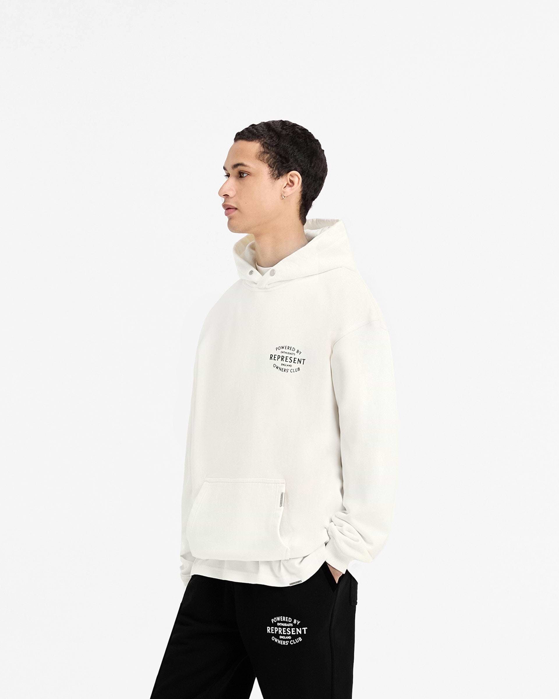 Man wearing a white hoodie on a plain white background | Represent Owners Club Stamp Hoodie in Flat White | Heavy weight hoodie with Cobrax popper and high build branding | Owners Club Hoodies | Represent Clo