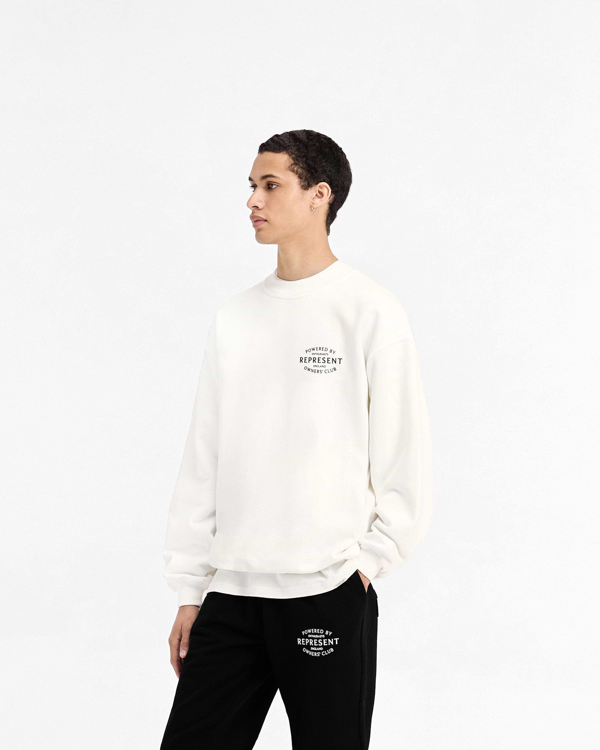 Man wearing a white sweater on a plain white background | Represent Owners Club Stamp Sweater in Flat White | Oversized fit cotton sweater with ribbed details | Owners Club Sweaters | Represent Clo