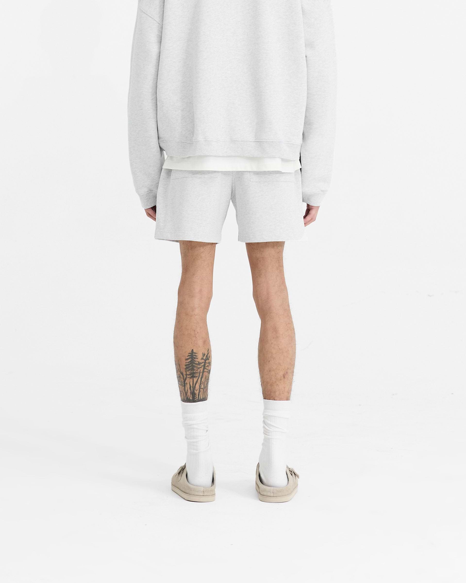 Man wearing grey sweatshorts on a plain white background | Initial Sweatshorts in Ice Grey Marl | Oversized boxy fit shorts with elasticated waistband and split hem | Initial Shorts | Represent Clo