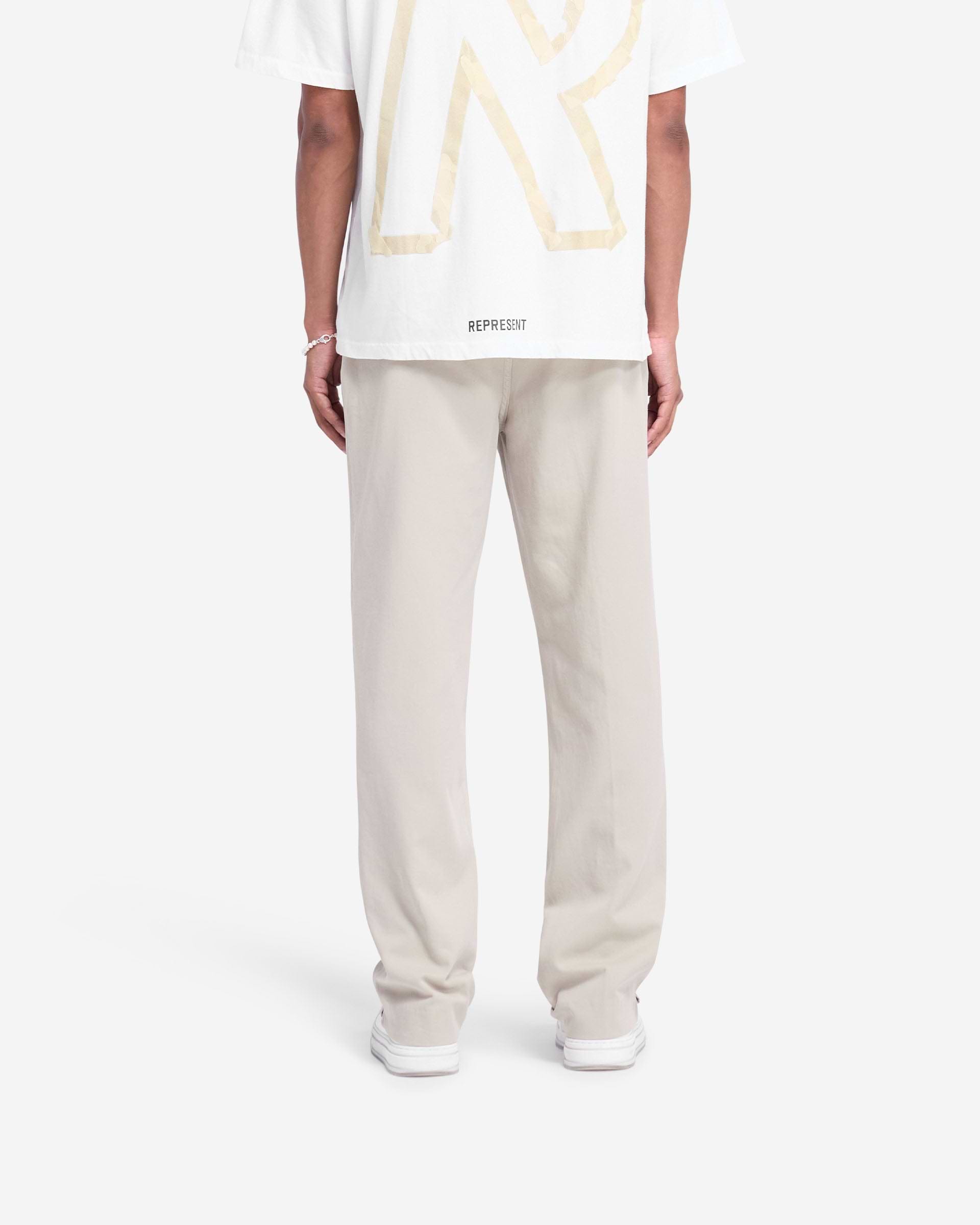 Man wearing stone cotton pants on a plain white background | Cotton Pant in Stone | Straight leg pants with twin needle rise and side pockets | FW24 Pants | Represent Clo