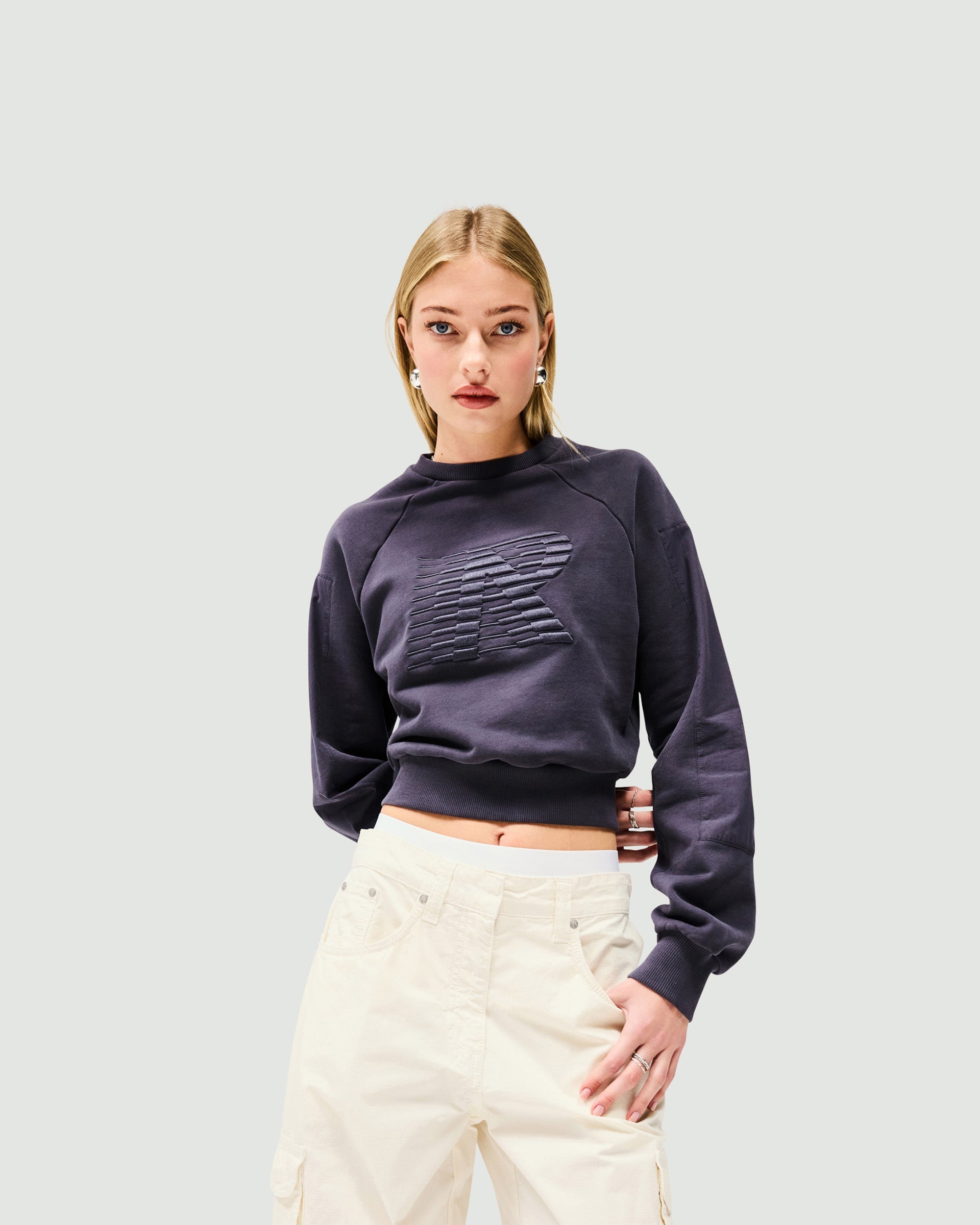 Woman wearing a grey long sleeve top on a plain white background | Reverse Long Sleeve Top in Washed Grey | Long sleeve top with racing Initial R logo | Womens SS25 Tops | Represent Clo