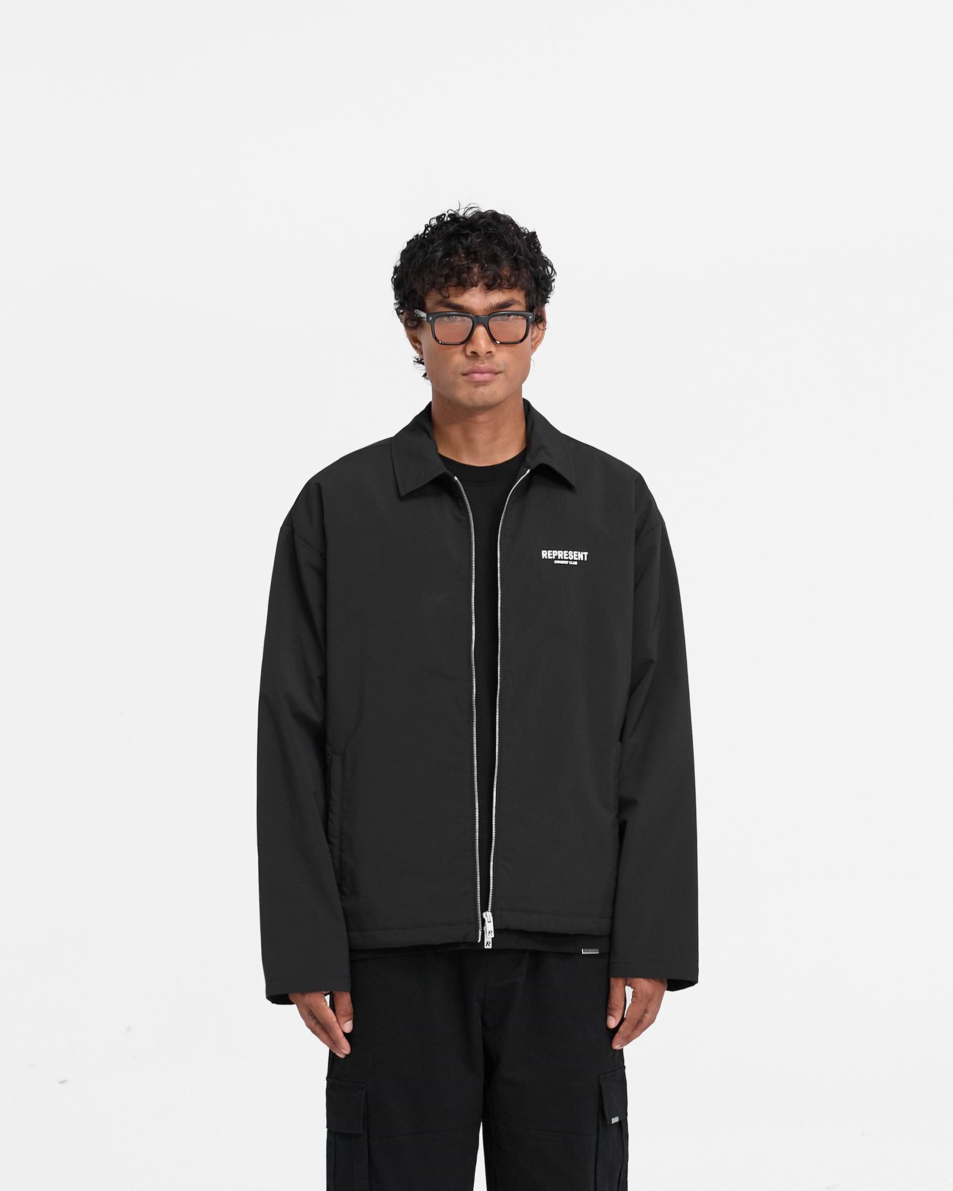 Man wearing a black coach jacket on a plain white background | Represent Owners Club Coach Jacket in Black | Regular fit jacket with lightweight sheet wadding | Owners Club Outerwear | Represent Clo