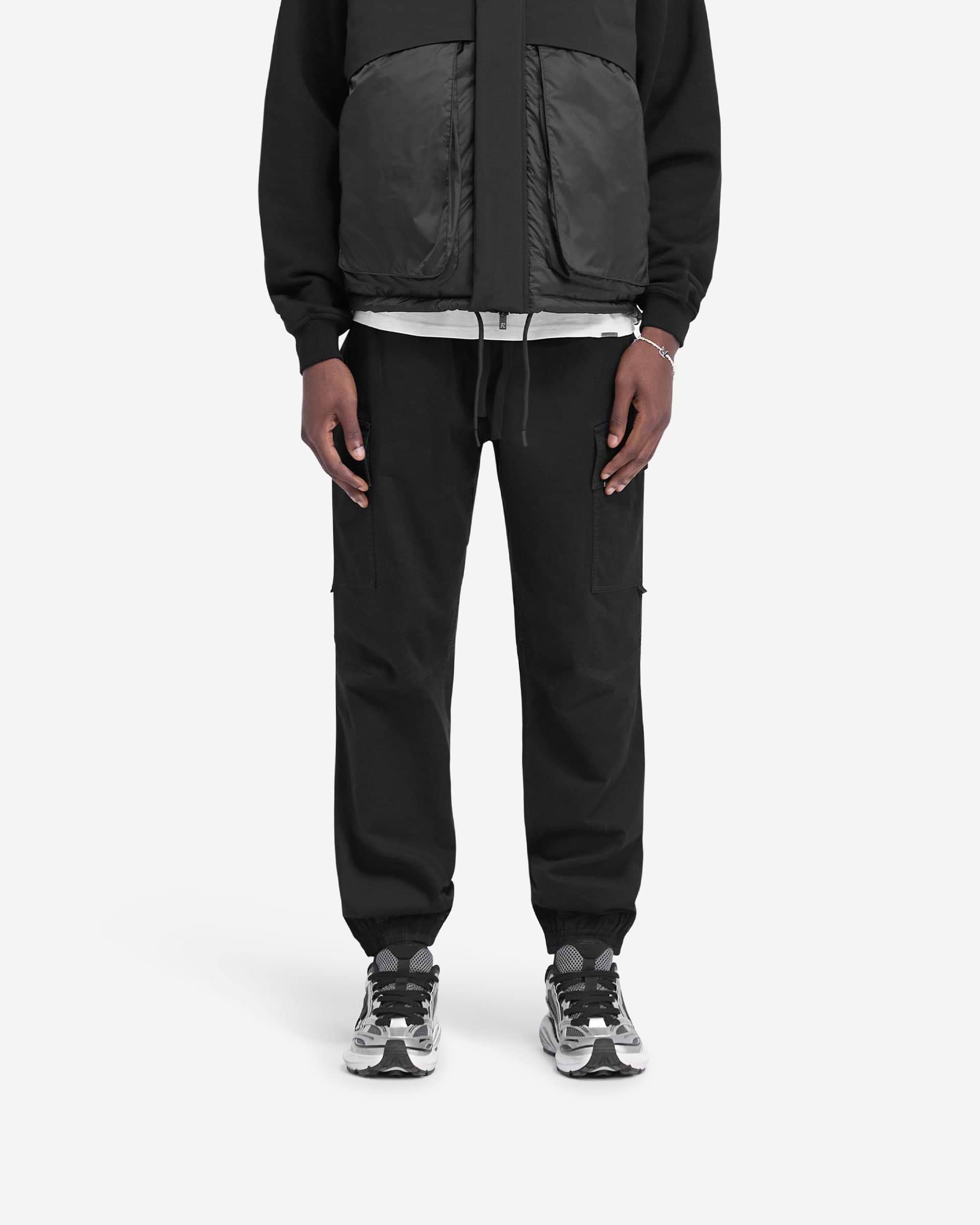 Man wearing black cuffed cargo pants on a plain white background | Cuffed Cargo Pant in Black | Cargo pants with elasticated waistband and cuffs | FW24 Pants | Represent Clo