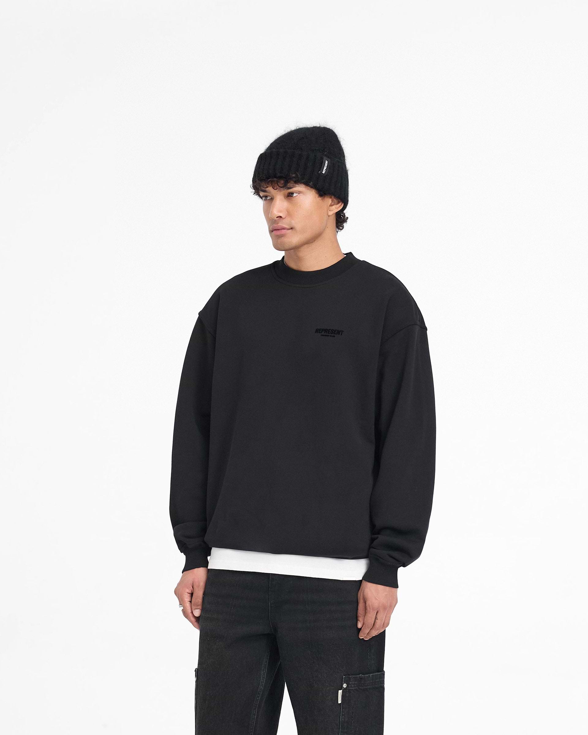 Man wearing a black oversized sweater on a plain white background | Represent Owners Club Flocked Sweater in Black | Heavy weight jersey cotton sweater with flocked print and ribbed trims | Owners Club Sweaters | Represent Clo