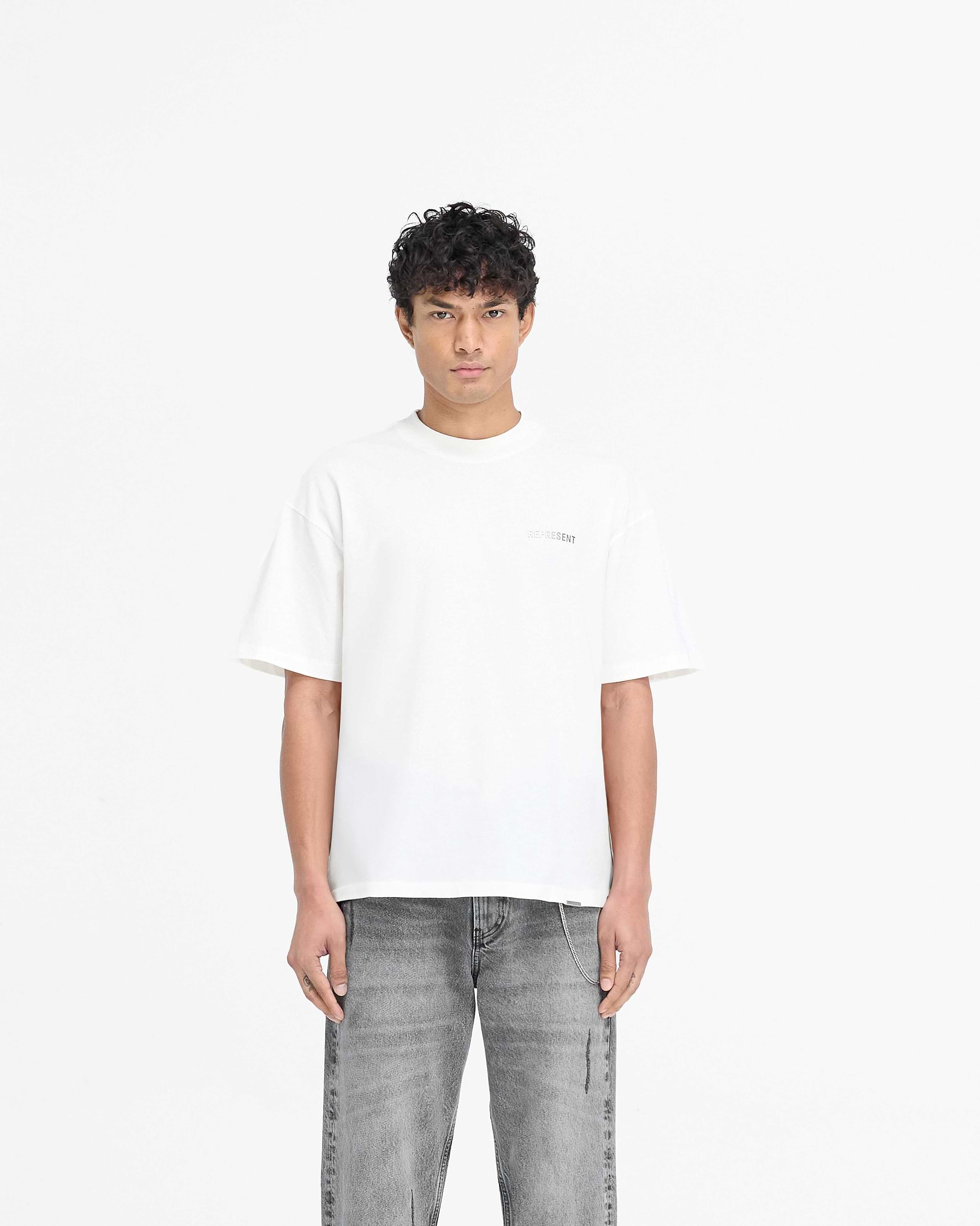 Man wearing a white t-shirt on a plain white background | Block Logo T-Shirt in Flat White | Slightly oversized t-shirt with metal branding | PRE SS25 T-Shirts | Represent Clo