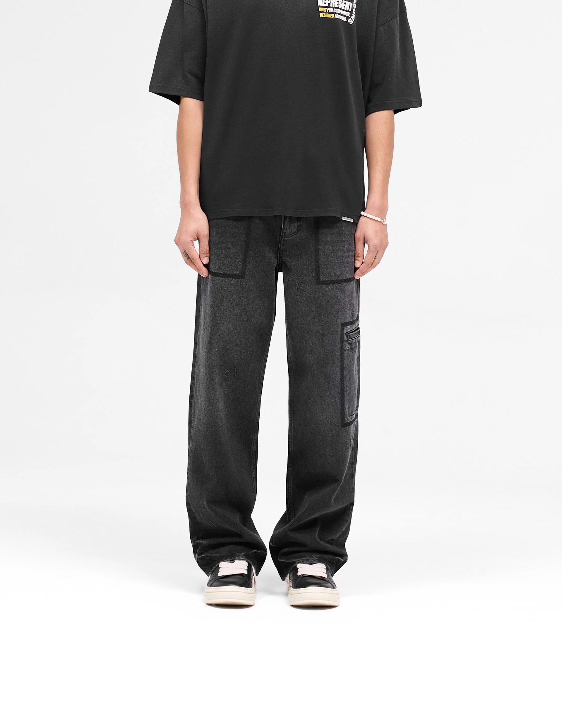Man wearing black denim jeans on a plain white background | R3 Drive Denim in Jet Black | Baggy fit jeans with distressed detailing | SS25 Denim | Represent Clo